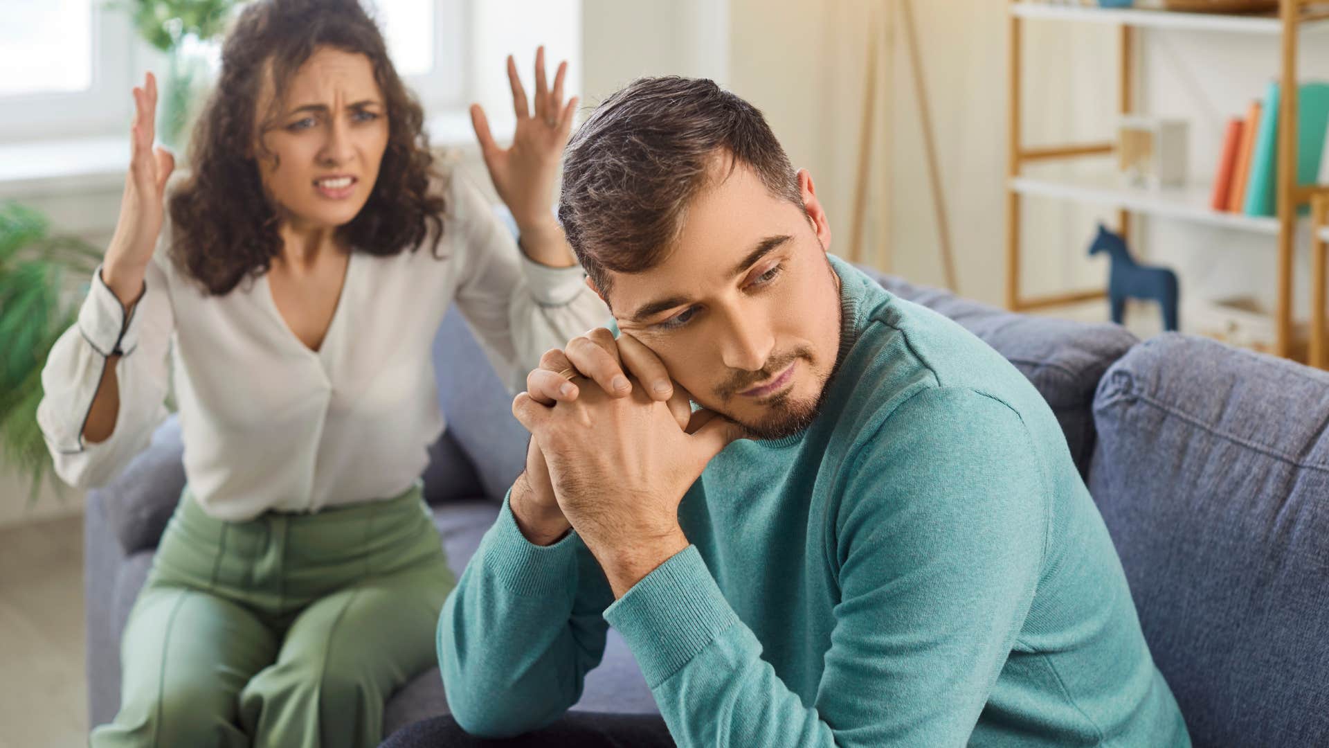 man sitting on couch looking away from upset wife