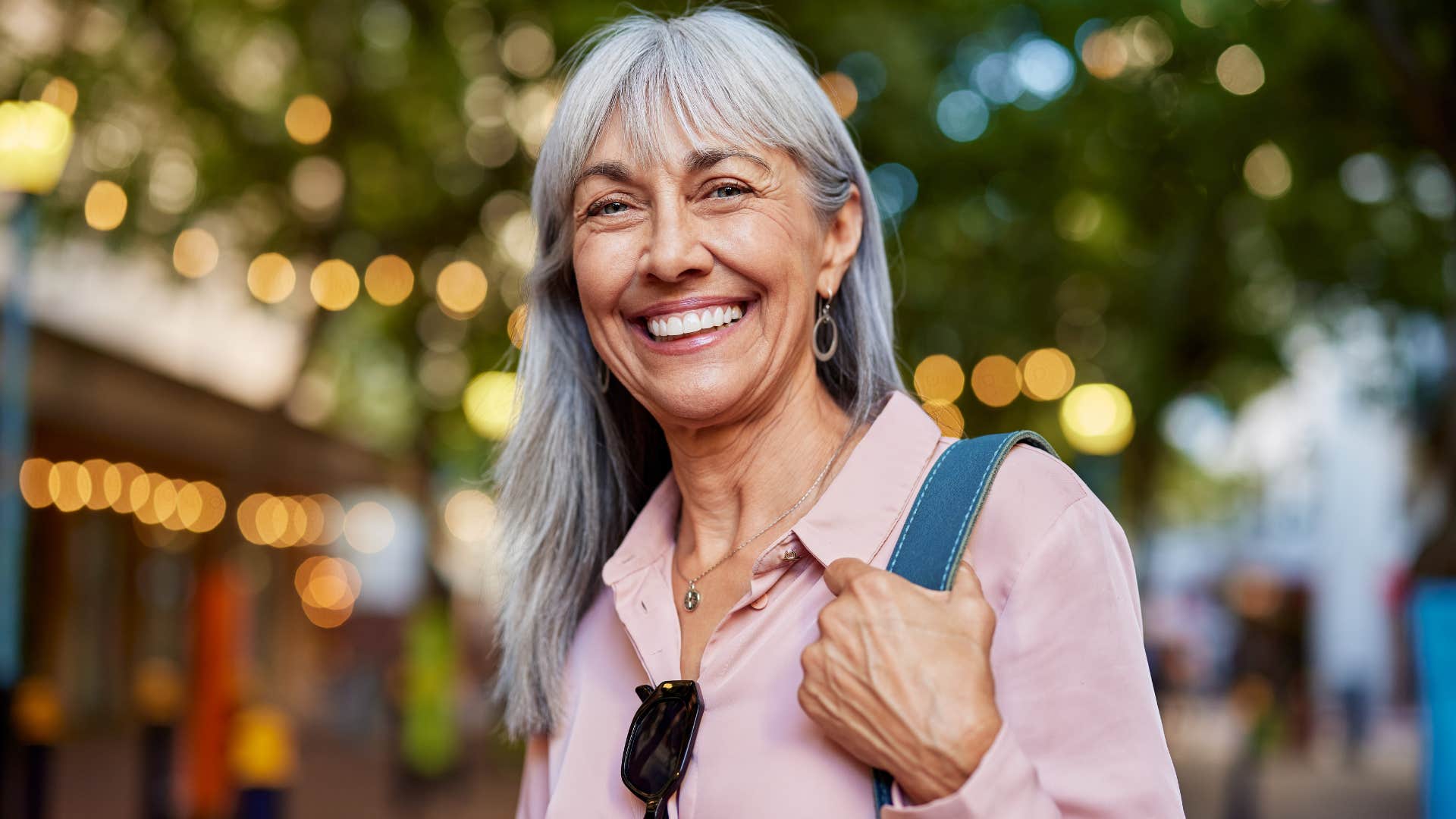 Older persn with shoulder bag smiles showing habit of never giving up