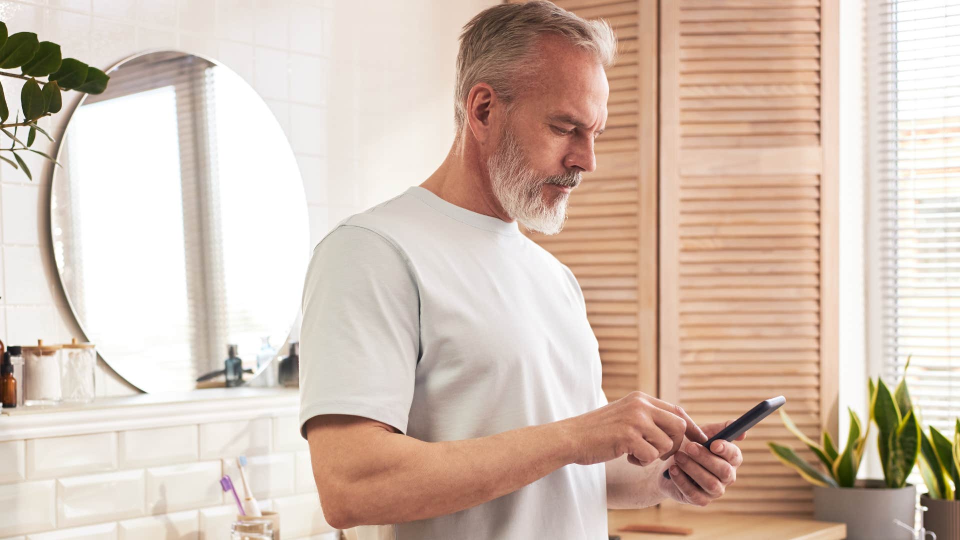 unhygienic man not washing his hands in the bathroom looking at his phone