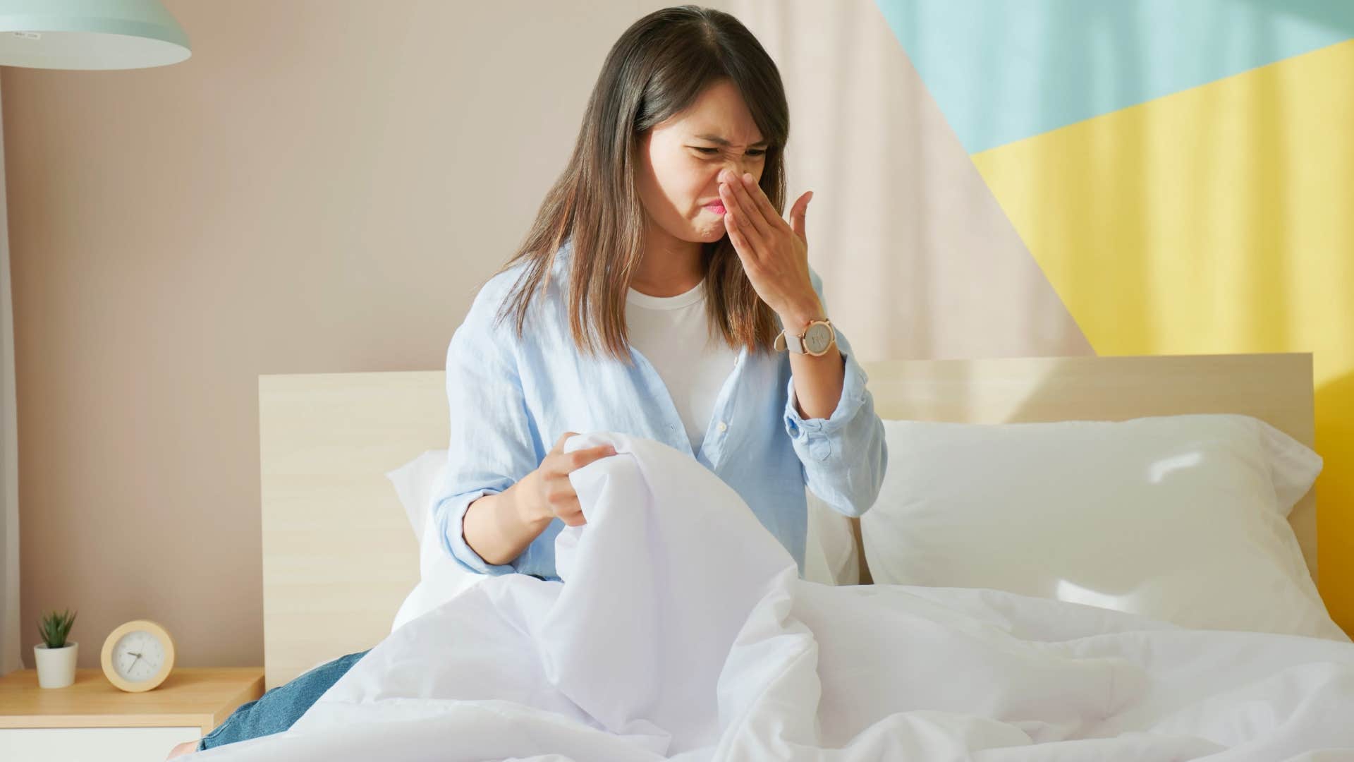 woman smelling odor after waiting too long to wash her bed sheets