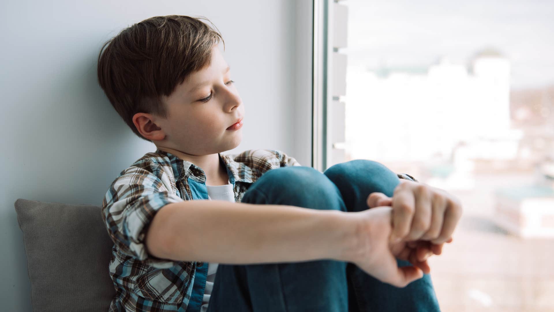 bored little boy sitting near window