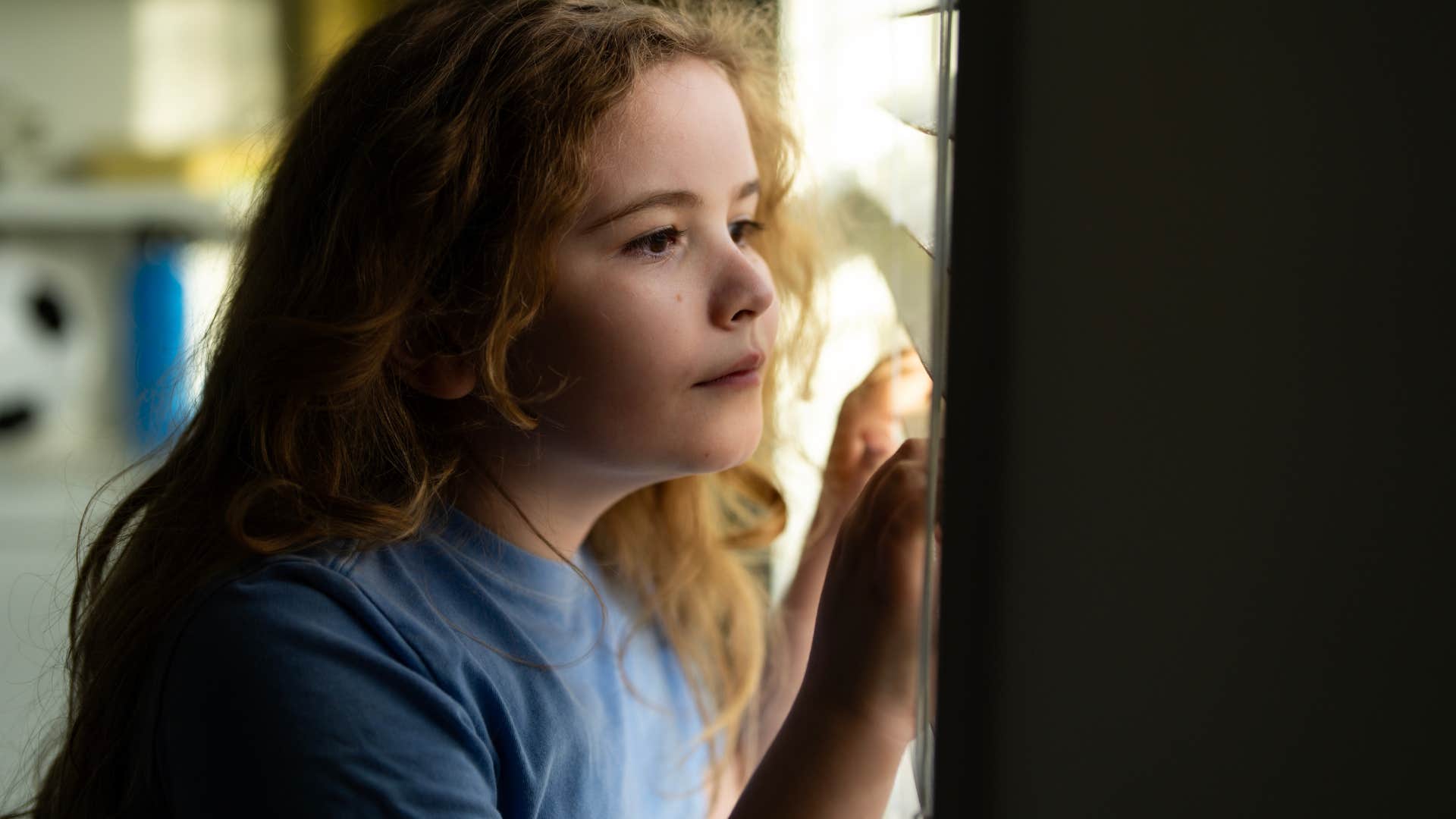 little girl looking through window at home