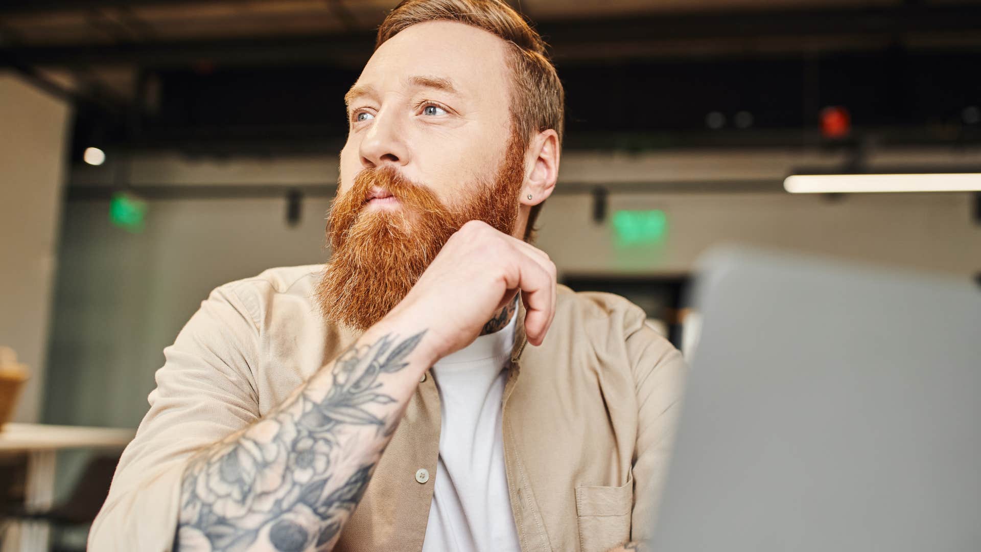 sentimental man with tattoos sitting at work pondering