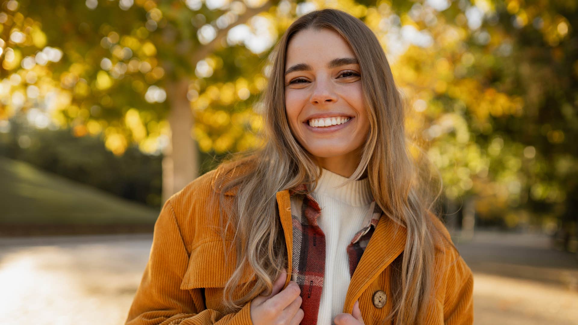 woman in orange jacket smiling brightly as she says i'd rather be real than liked