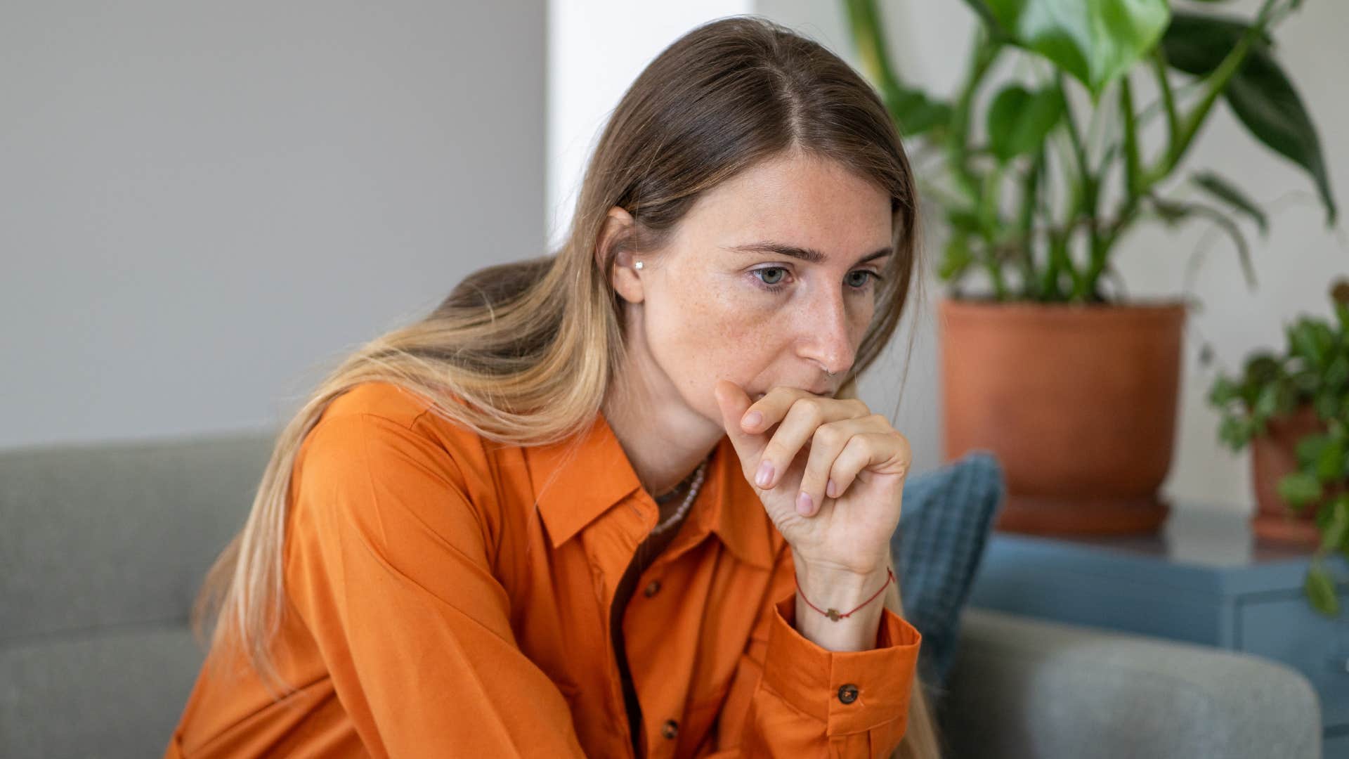 woman in orange shirt thinking on couch i can't ignore my gut feeling