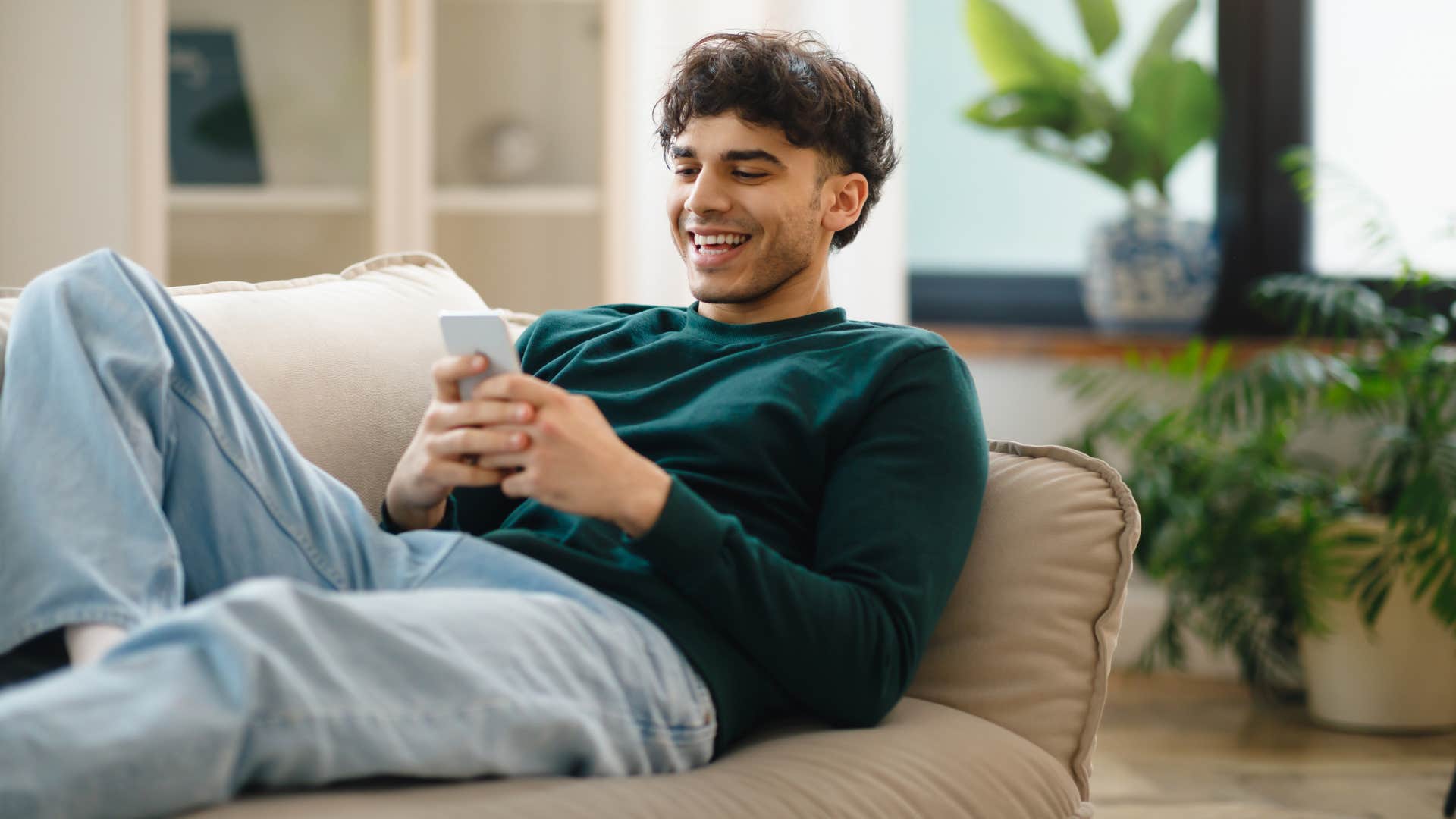 man in green sweater on couch and phone as social interactions are becoming more digitalized