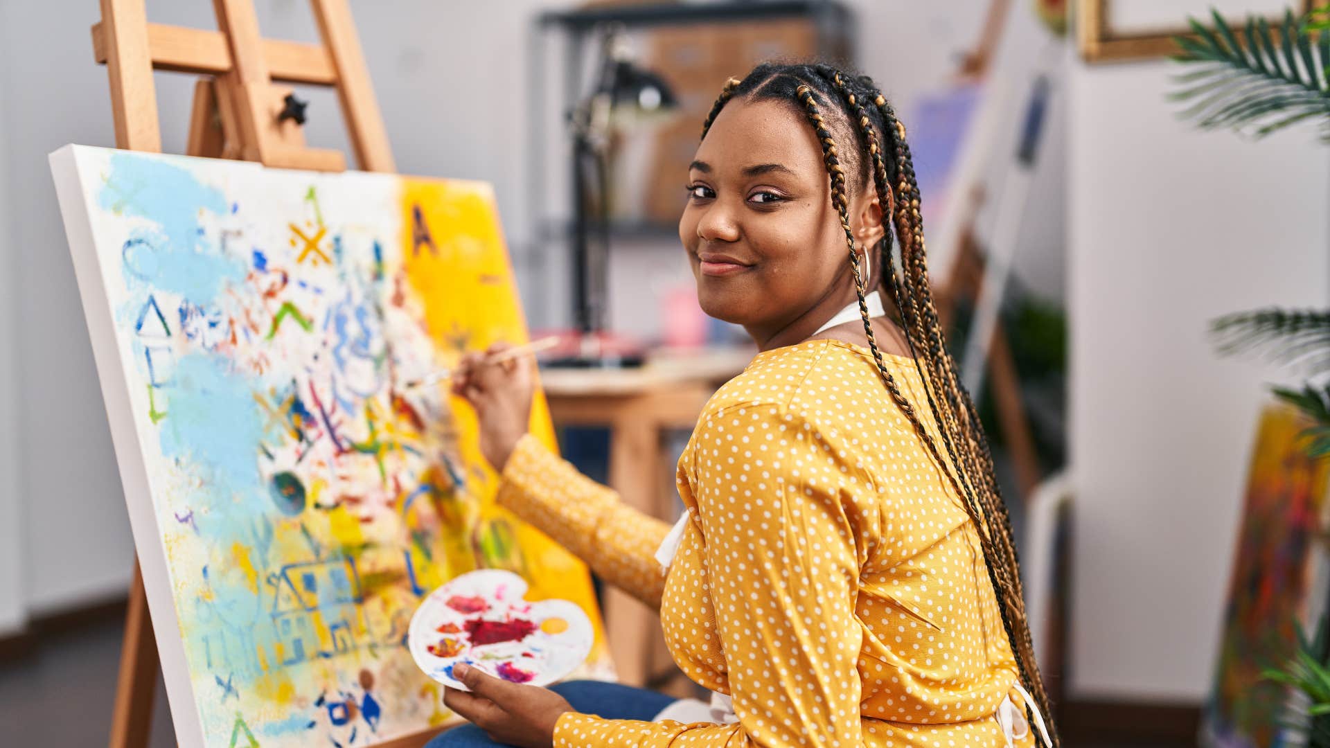 creative woman smiling while painting on canvas