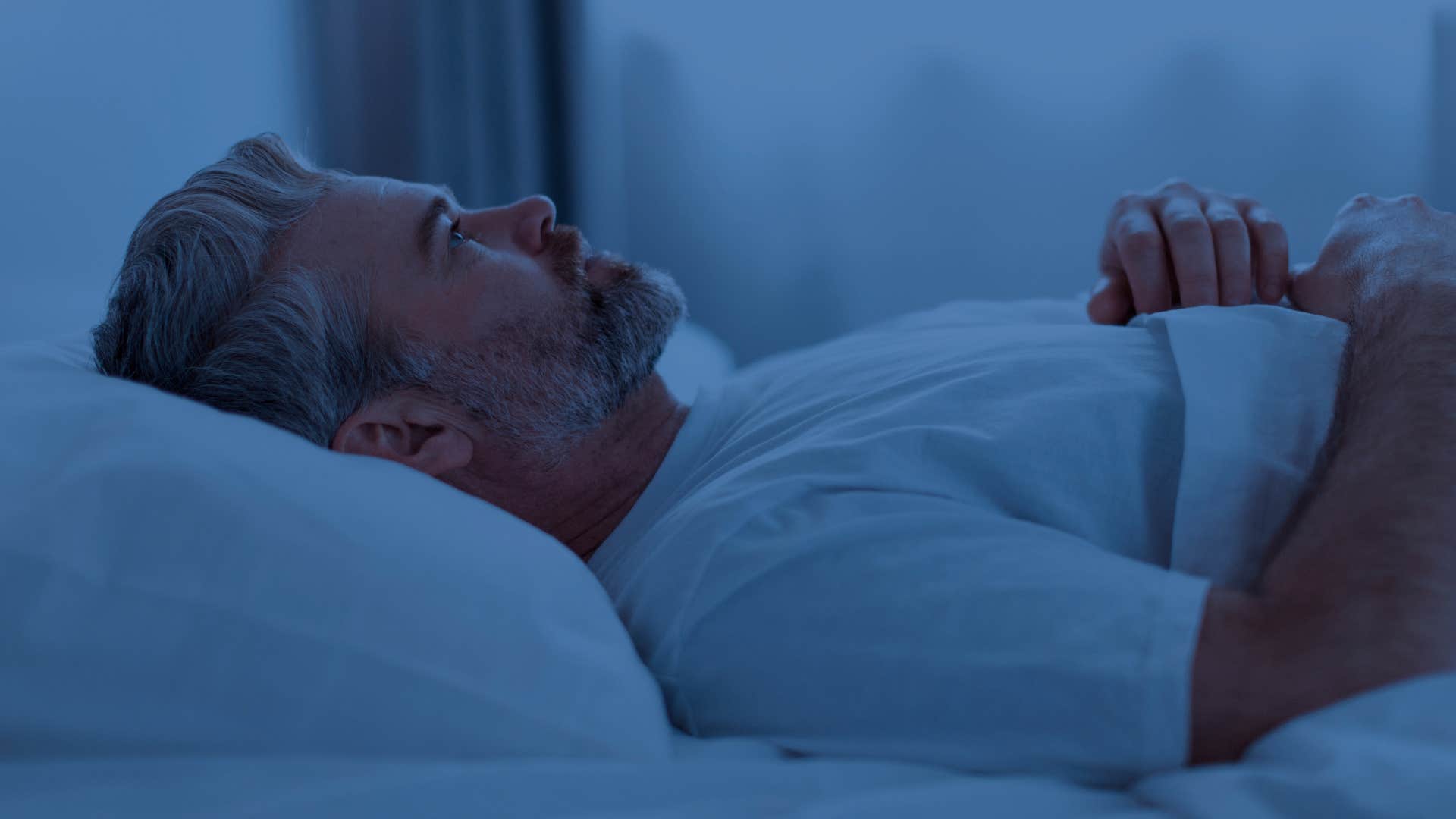 stressed man waking up often during the night lying in bed