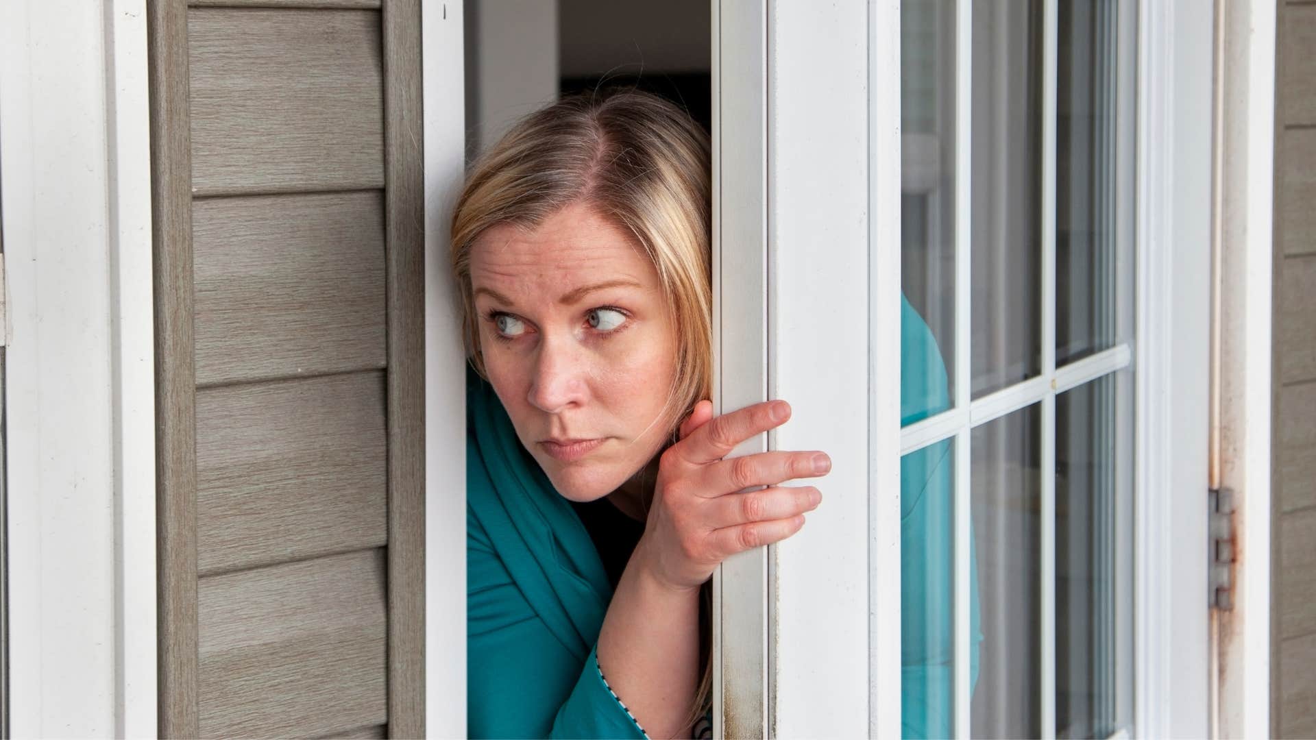woman in blue shirt coming out of the door extremely cautious 