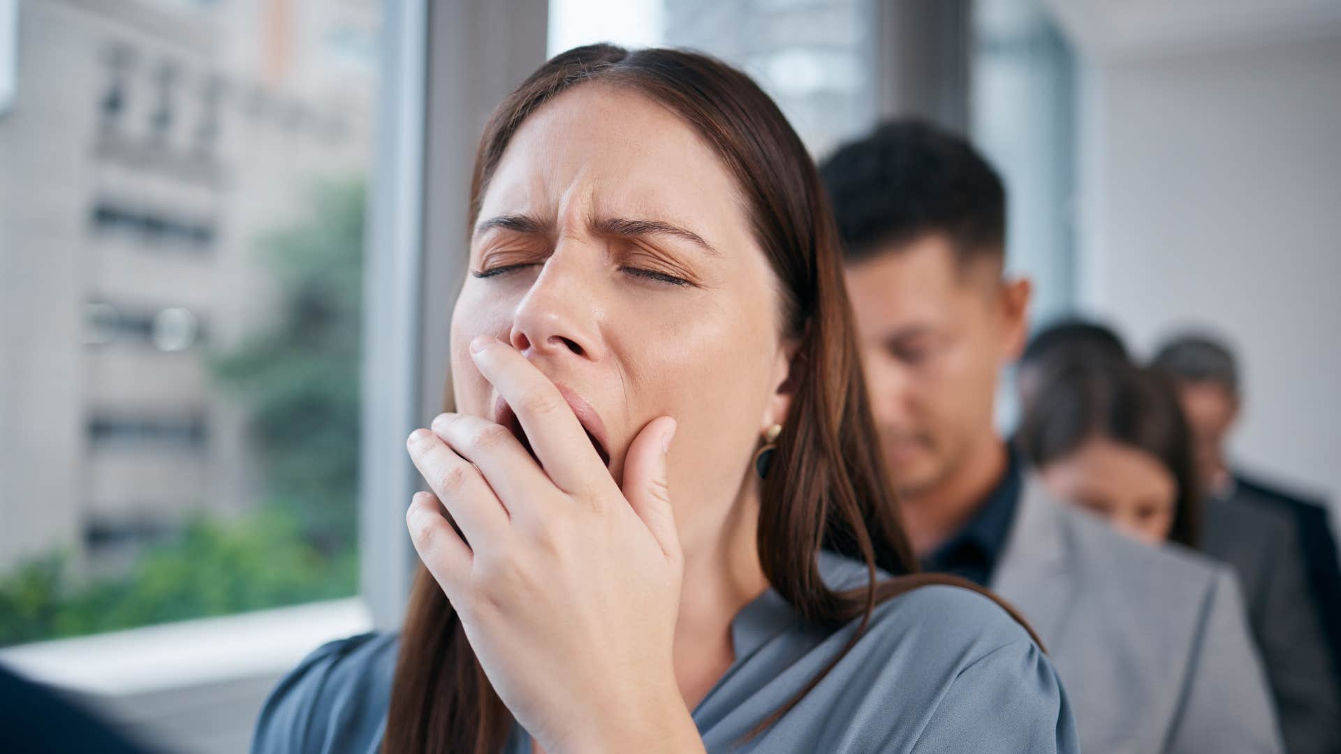 woman who is always tired yawning waiting in line