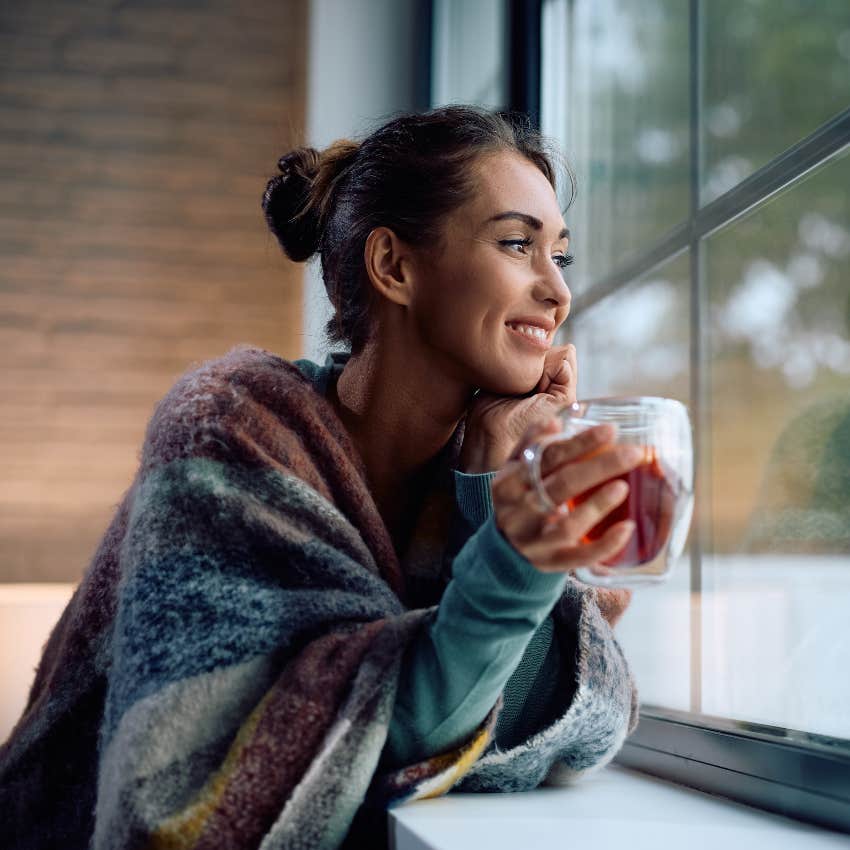 smiling woman looking out window keeping a positive outlook thanks to the burnt toasts theory