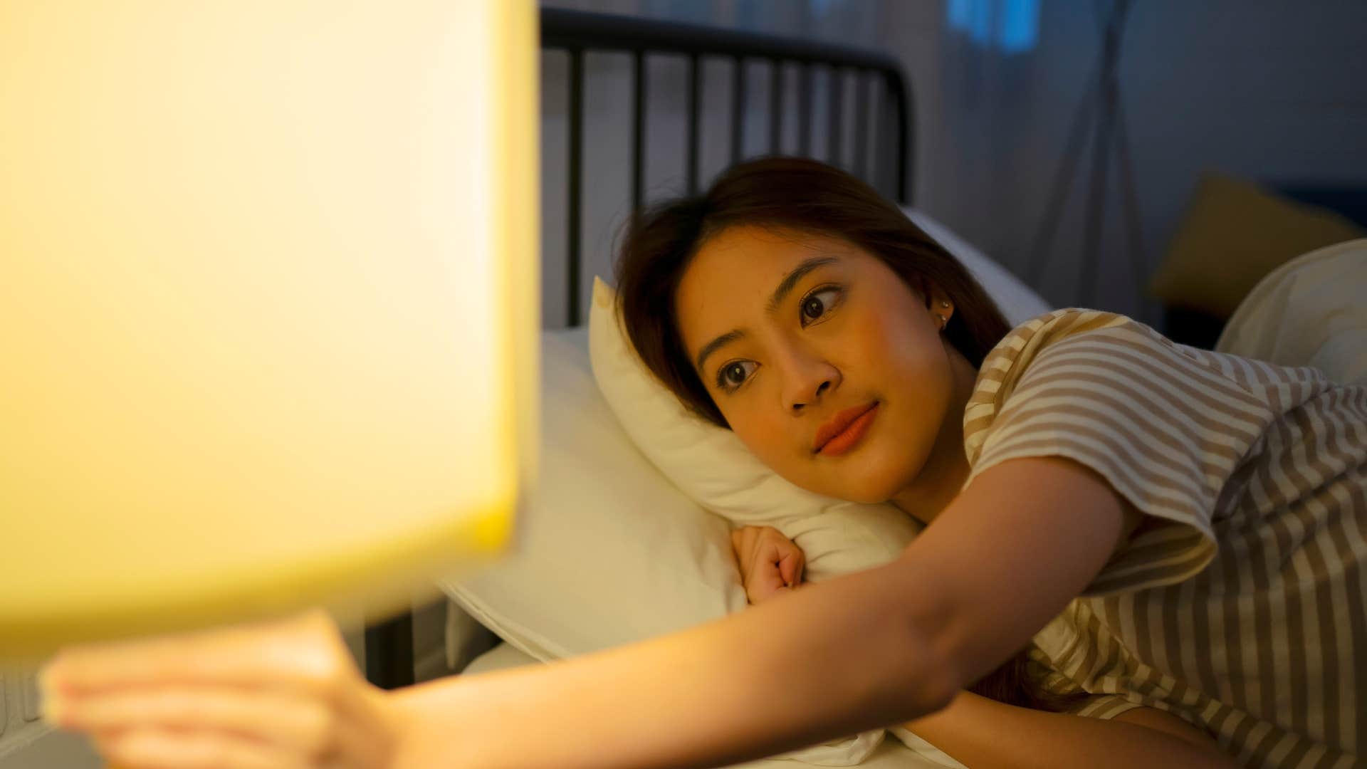 woman with reliable electricity turning on light laying in bed