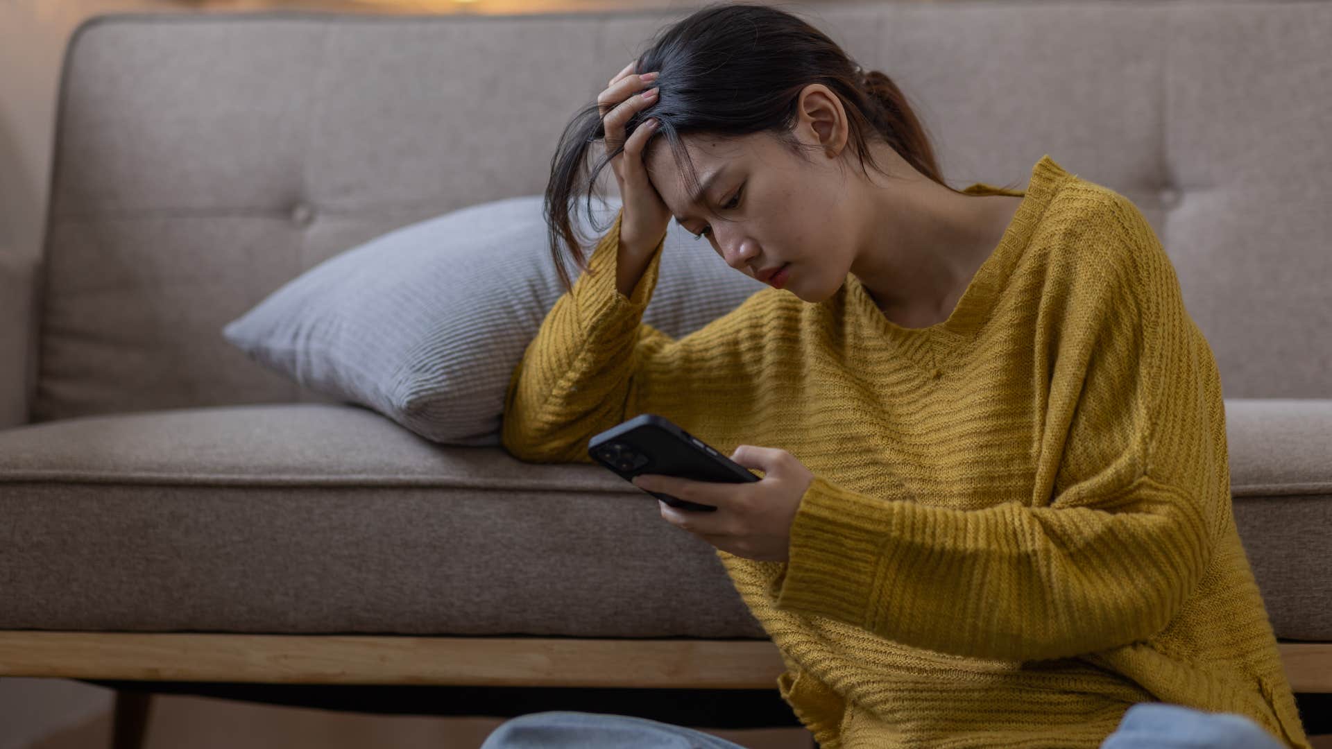 woman in yellow shirt doesn't feel safe inviting guests over as she looks at phone stressed