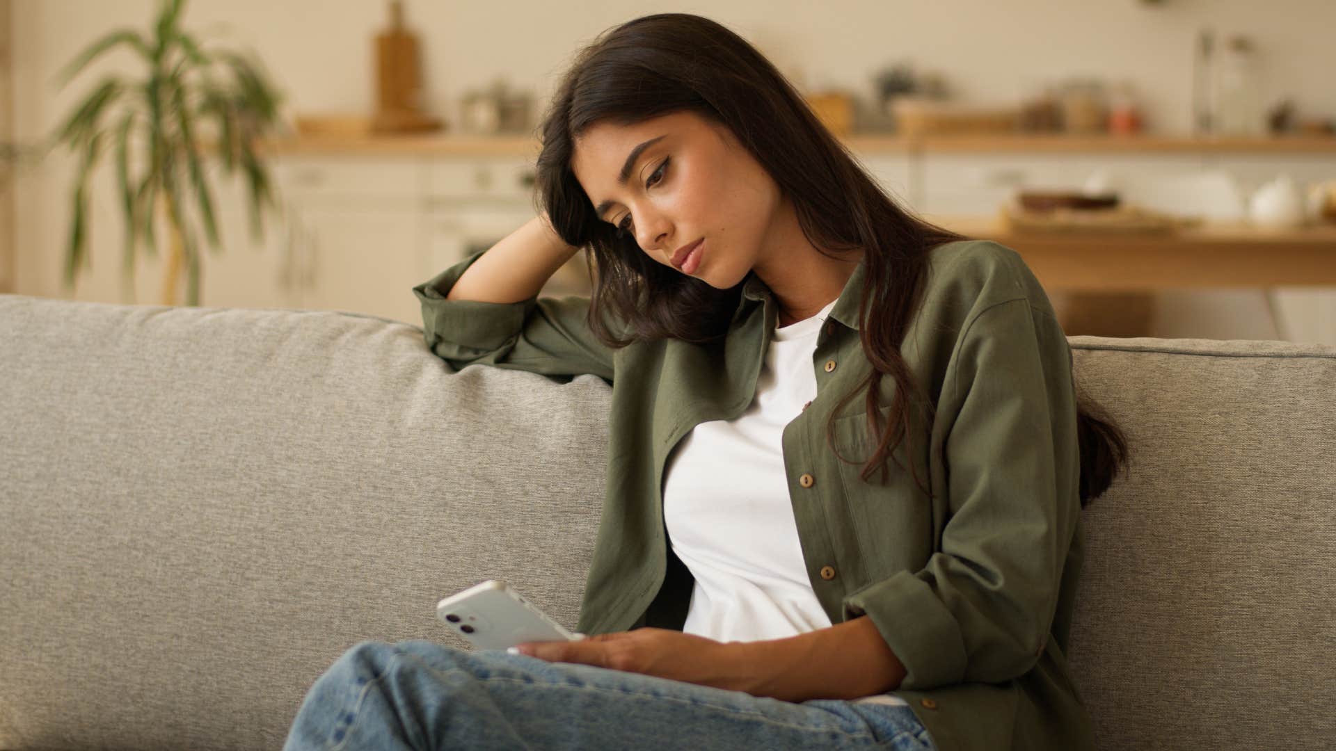 woman in green jacket still feels like they're passing through life as she stares at phone