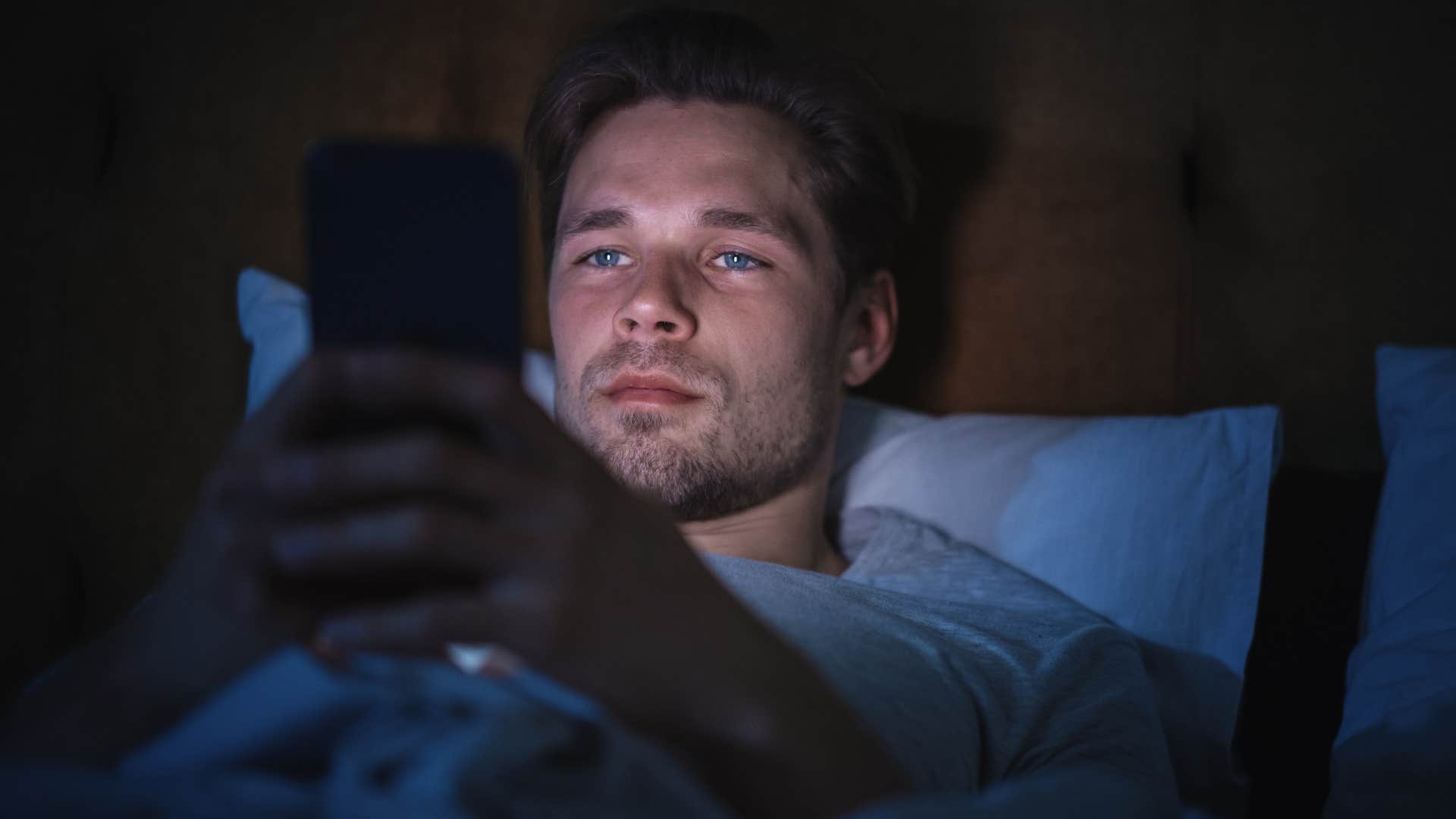 man who rarely relaxes on his own scrolling phone from bed