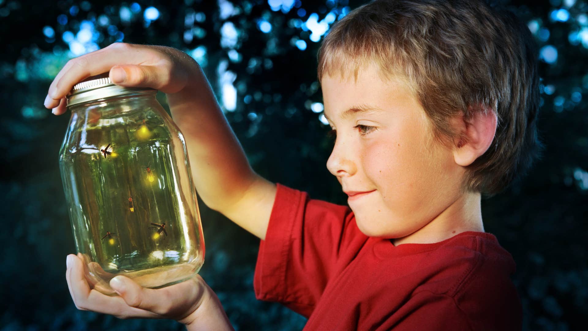 little boy catching fireflies in jar after school at dusk