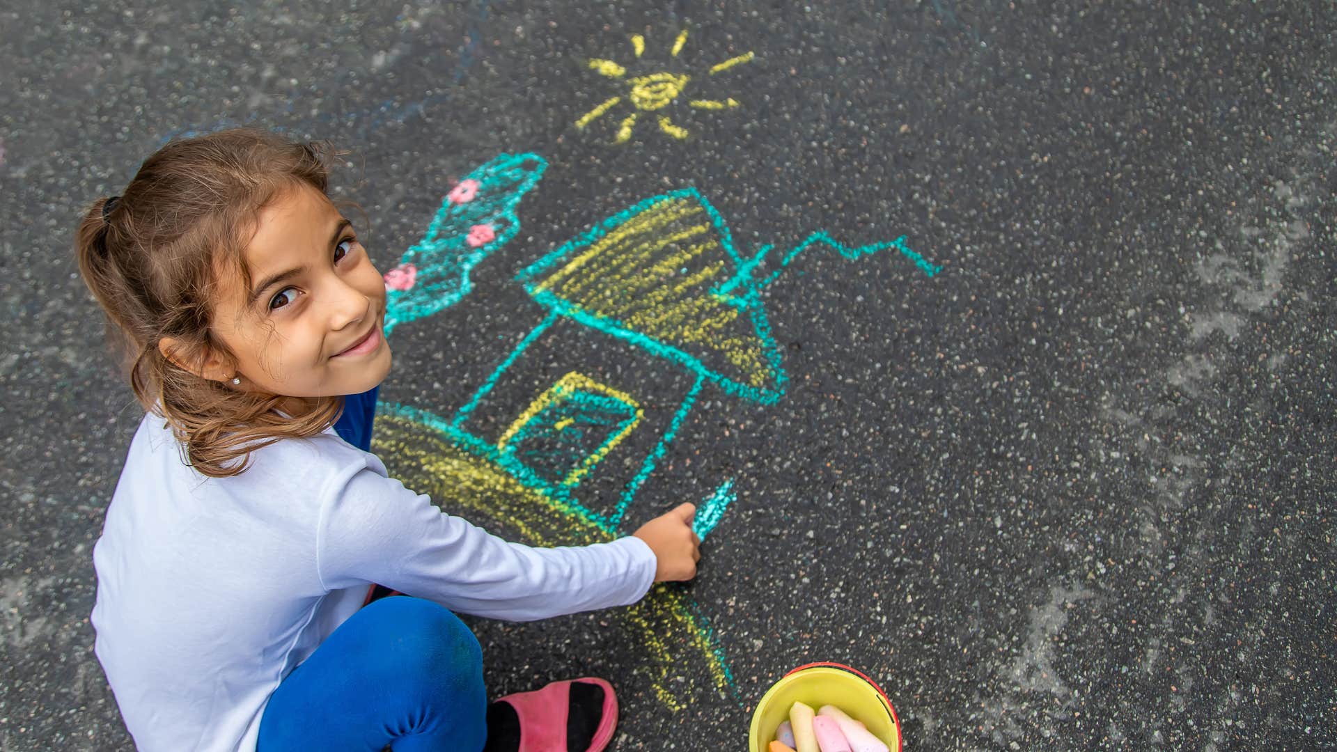 little girl drawing on sidewalk with chalk after school