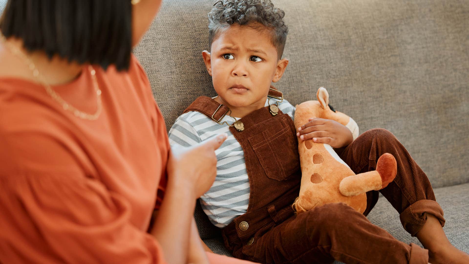 mom disciplining young son for bad behavior sitting on couch at home