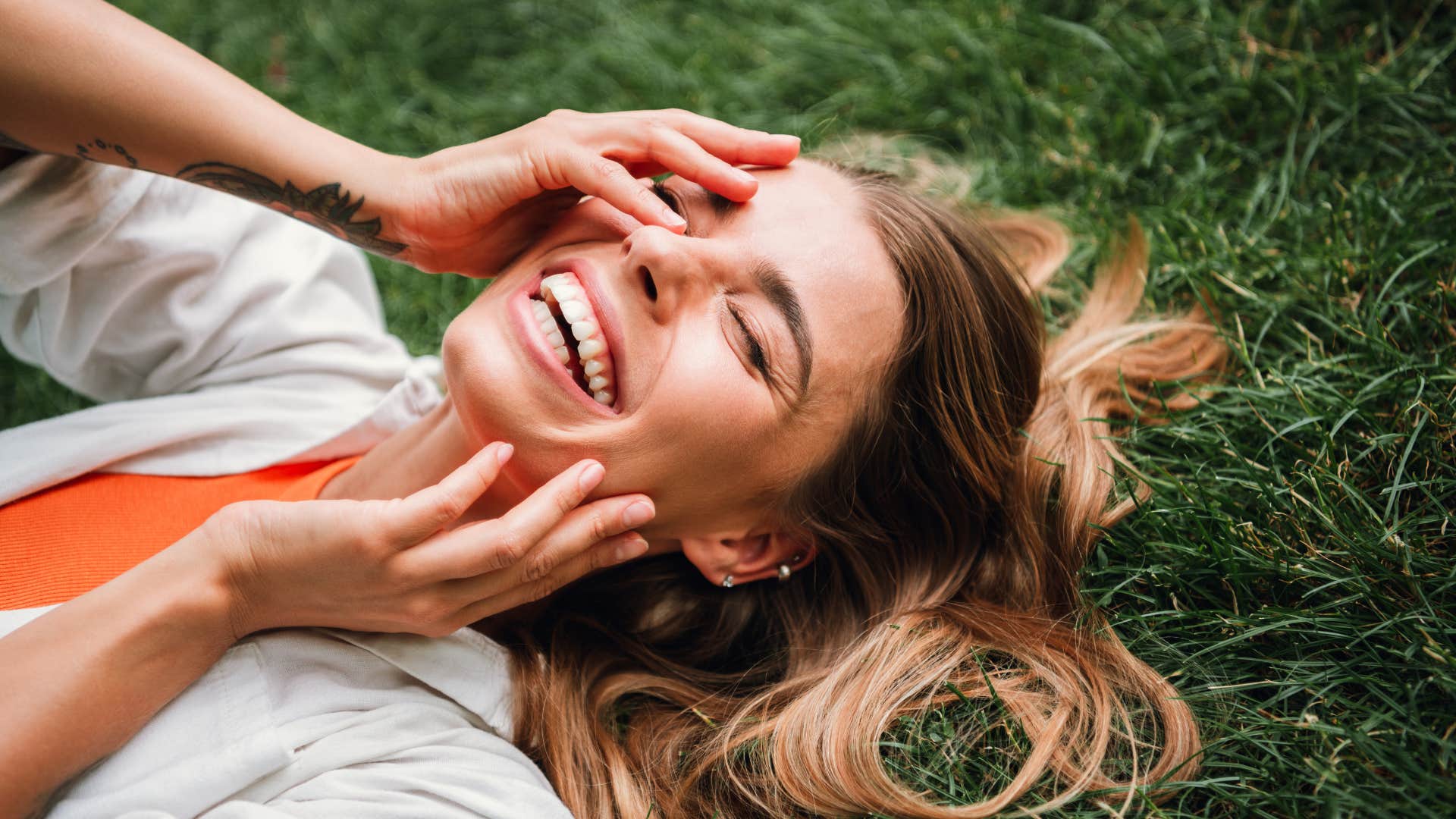 woman smiling laying on grass as she's the toxic optimist