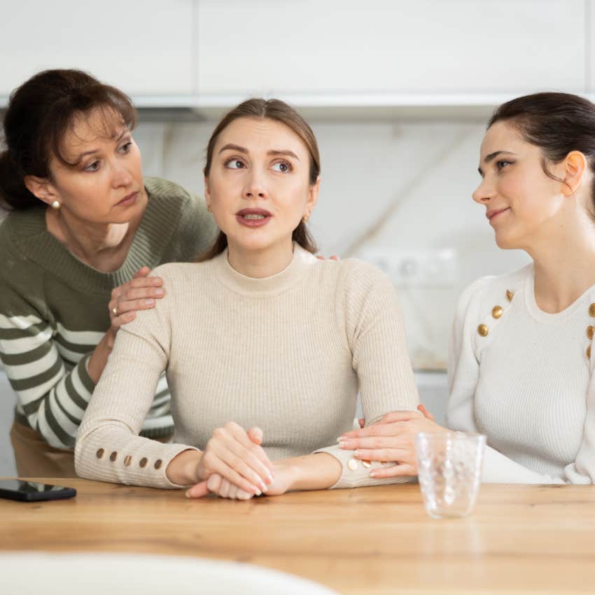 two women touching friend sitting at table