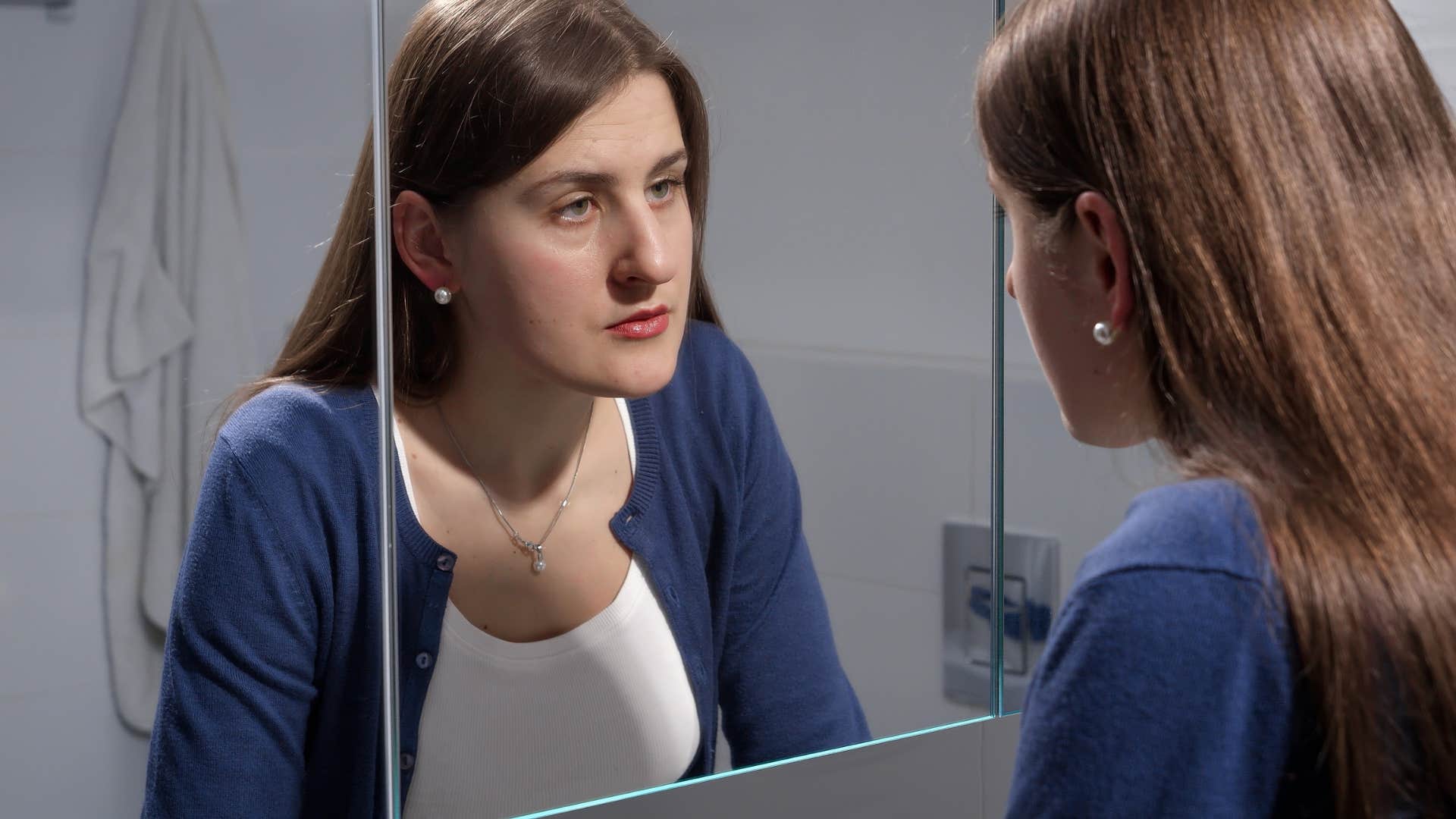 woman looking in the mirror being highly critical of herself