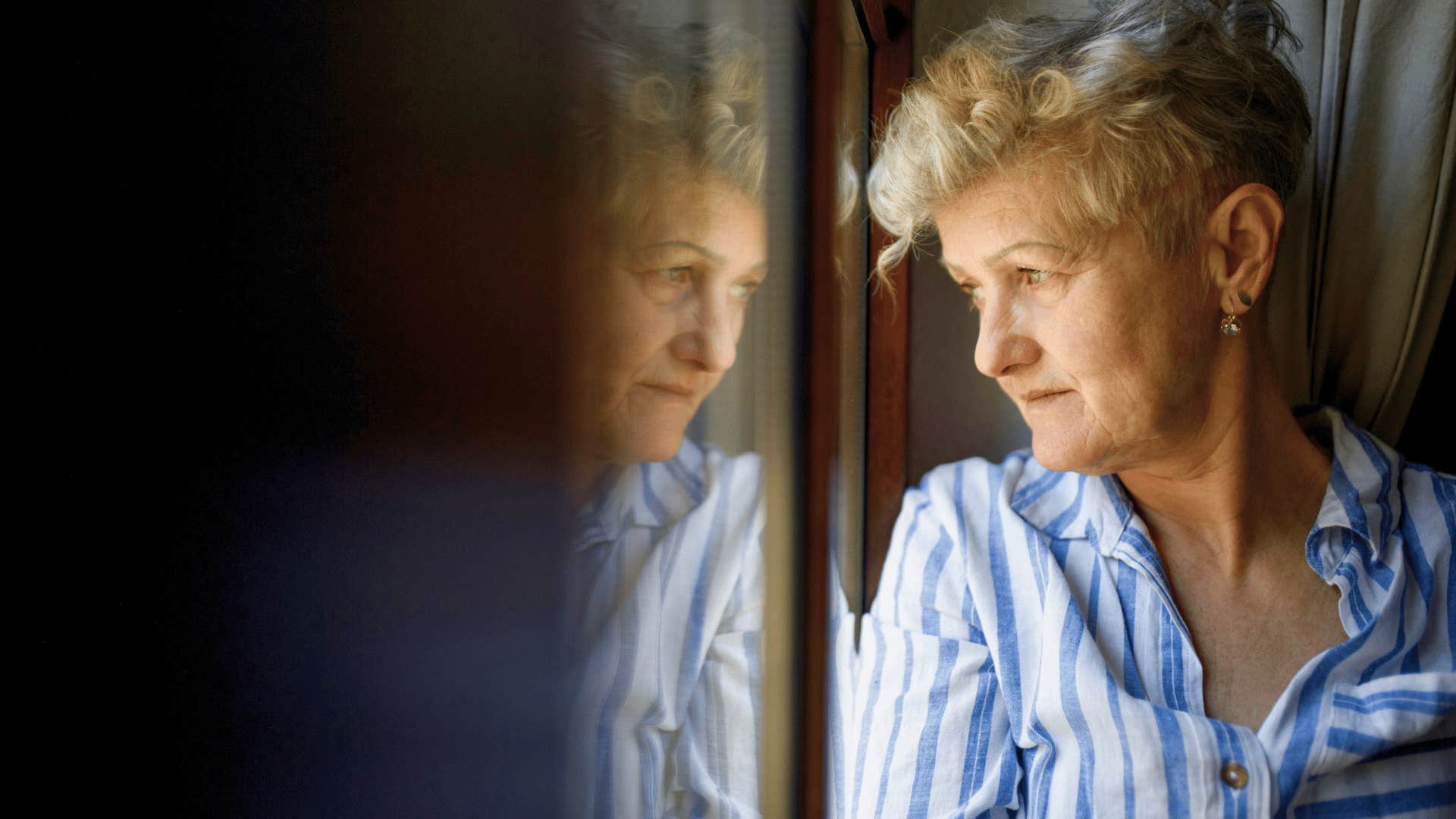 older woman looking out of window regretting being overobedient