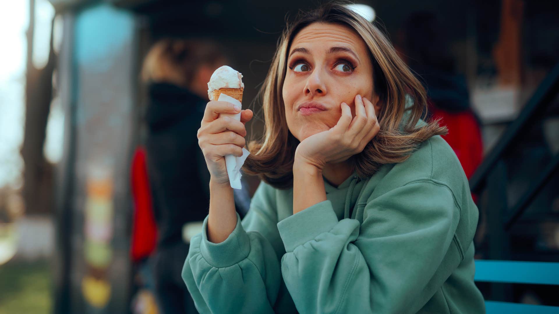 woman in green hoodie daydreaming as she eats standing up