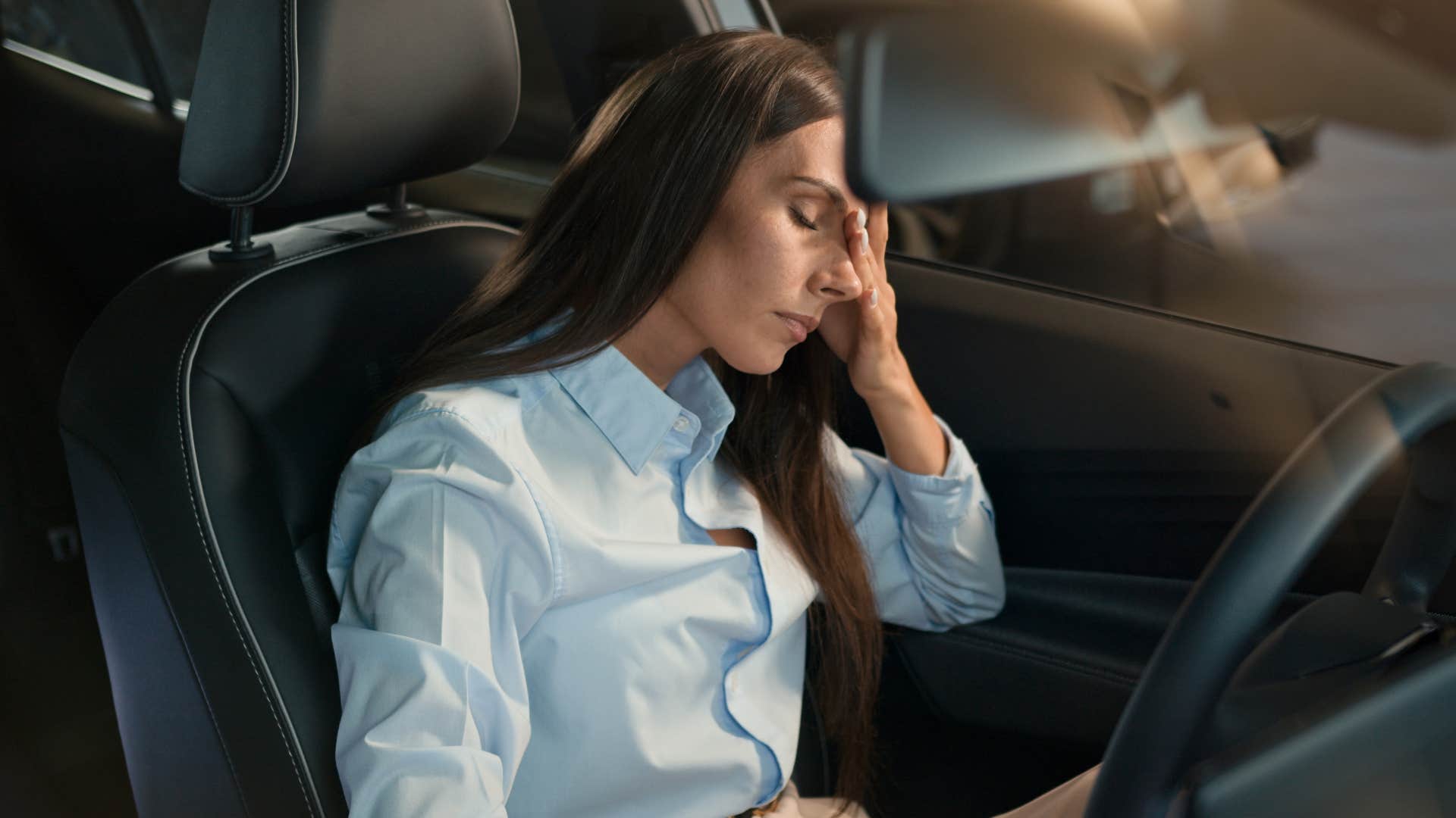 woman clutching head exhausted as she sits in her car for a few extra minutes