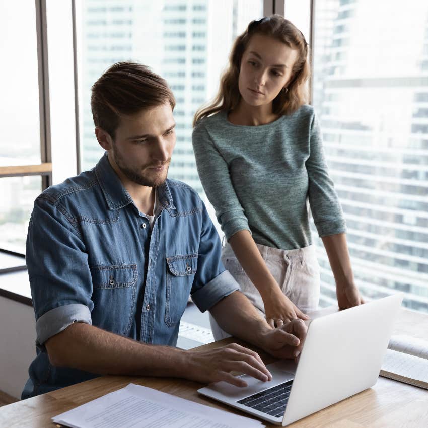 female boss looking over male worker's shoulder in office