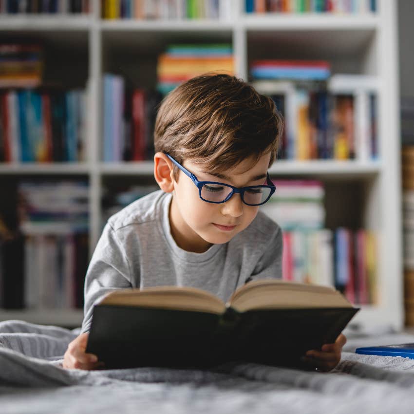 young boy with glasses reading book on bed developing traits carry into adulthood