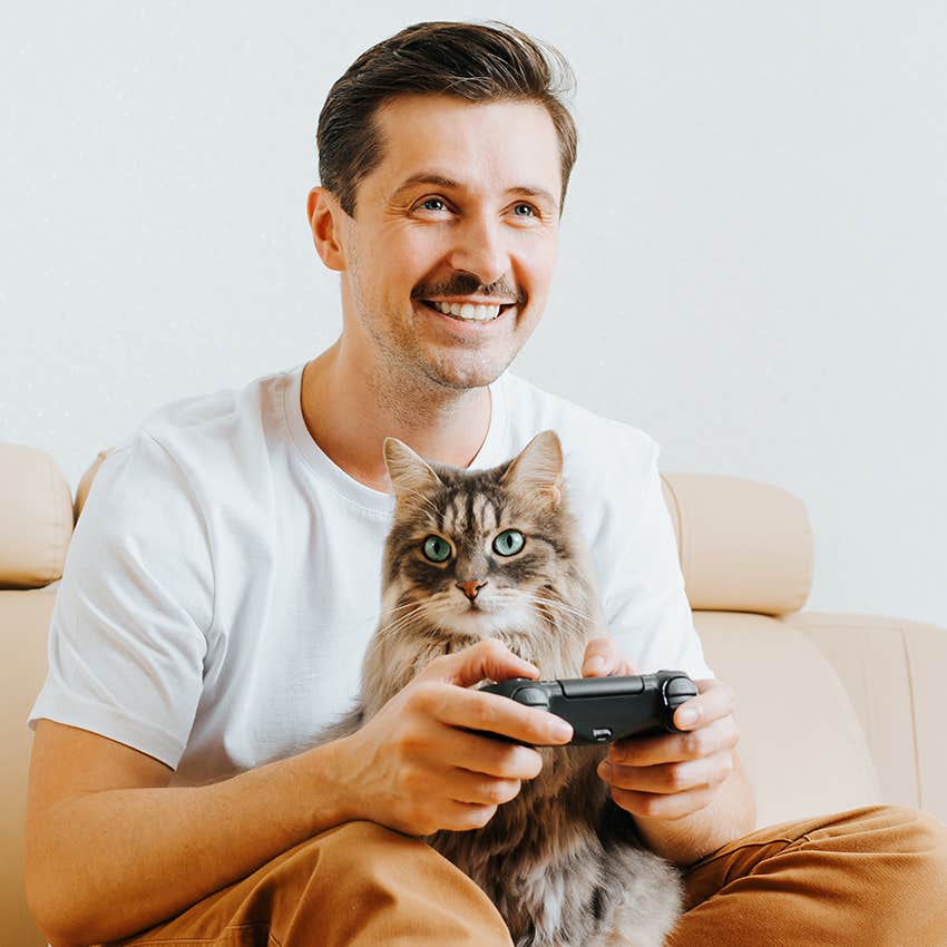 man happily playing video games with cat 