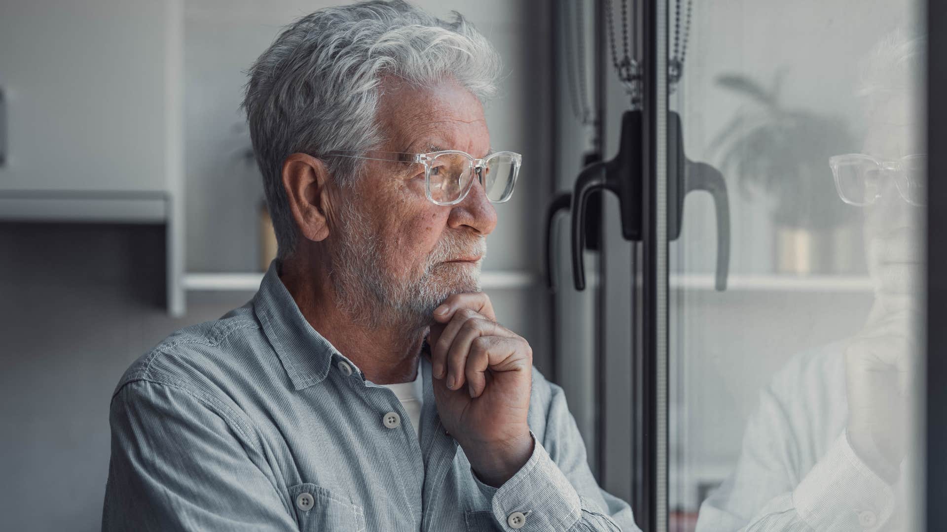 older man looking out a window feeling lonely and saying the house gets so quiet
