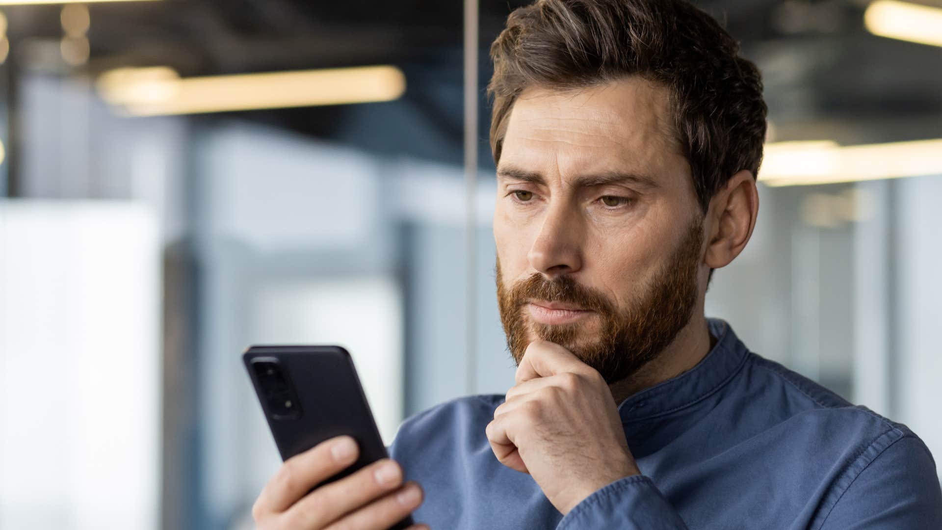 incredibly immature man looking at his phone at work