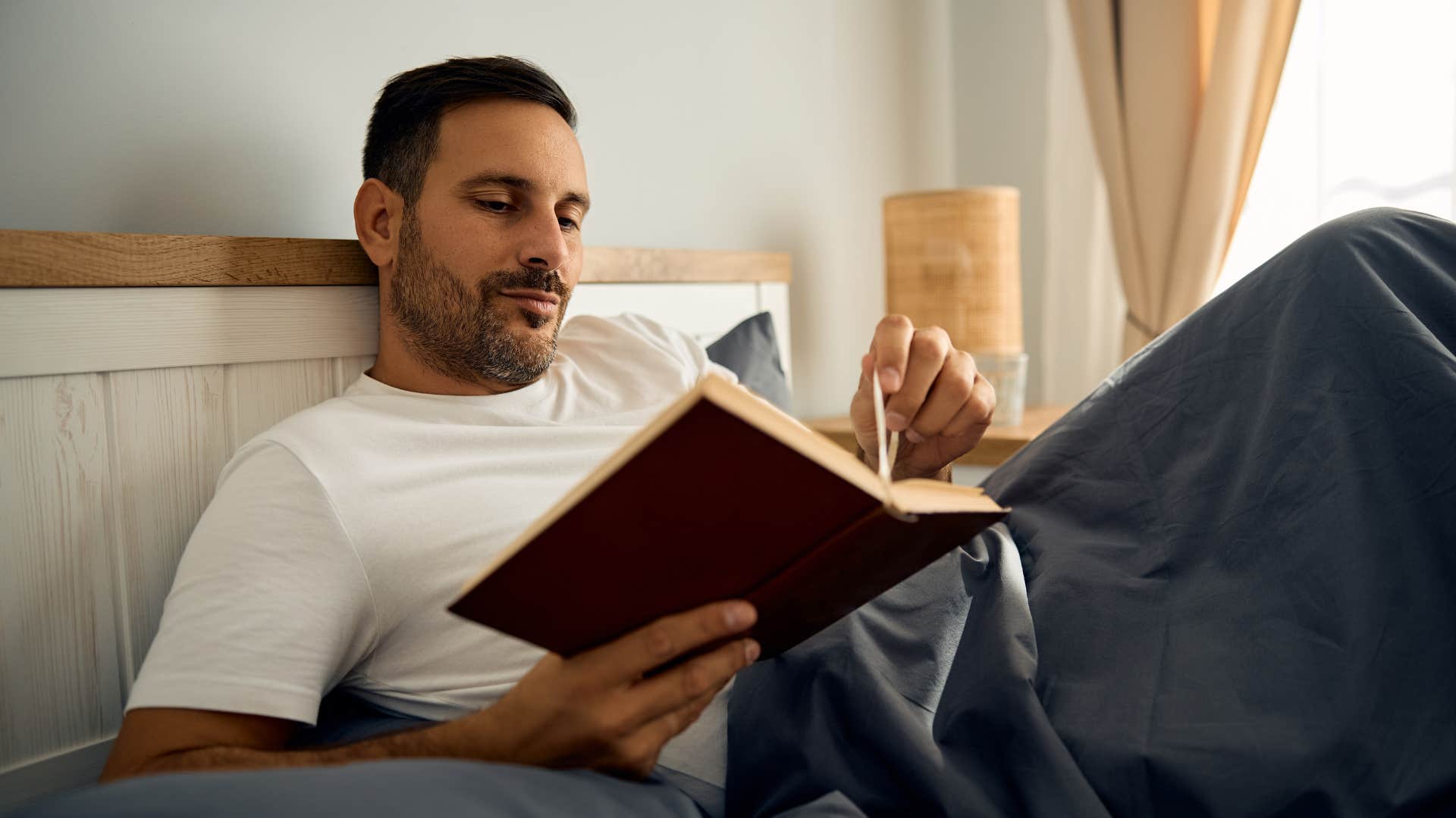 man laying in bed reading book instead of using social media