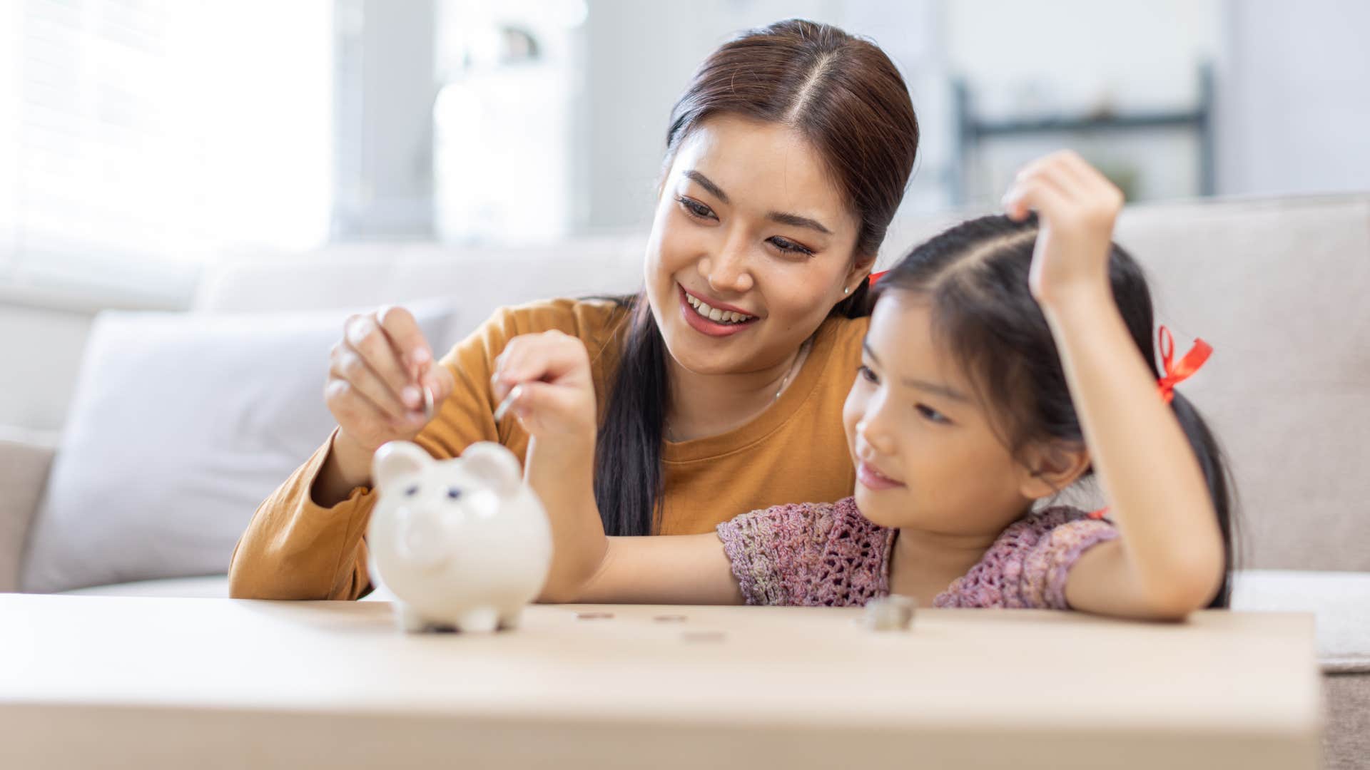 woman teaching her daughter to save money in piggy bank