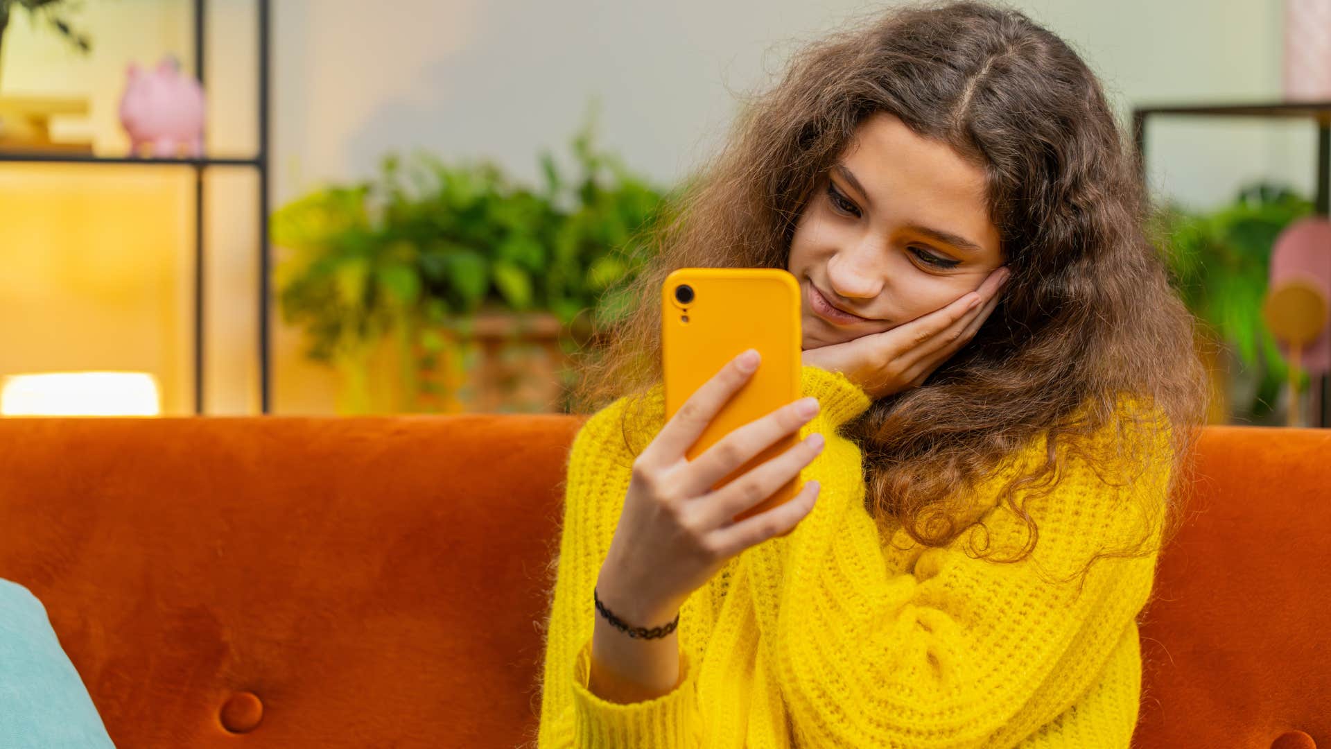 teenager in yellow sweater on expensive phone as she messes with the gadget on the couch