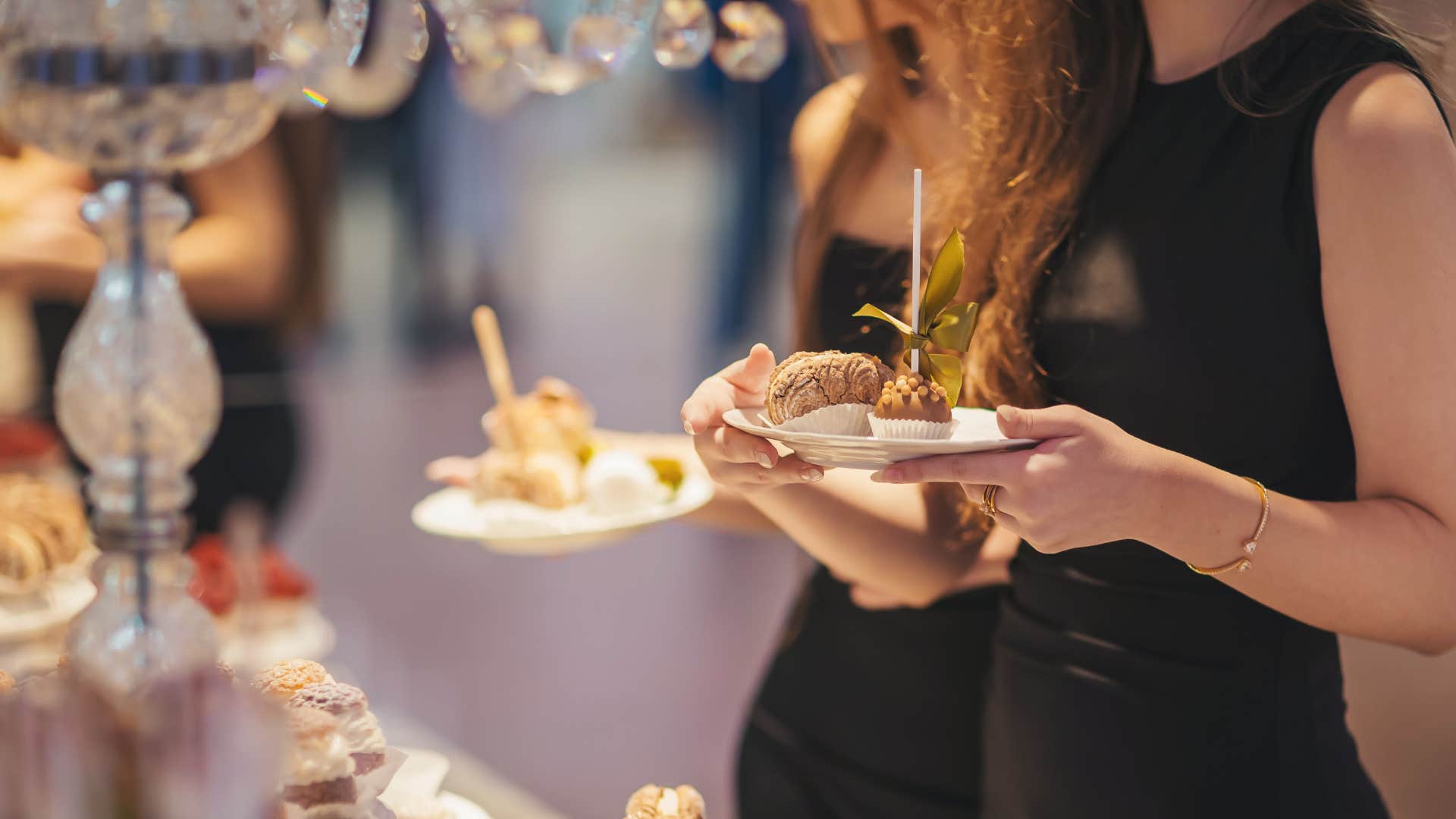 two women in black dress throwing lavish party every year as they grab treats from table