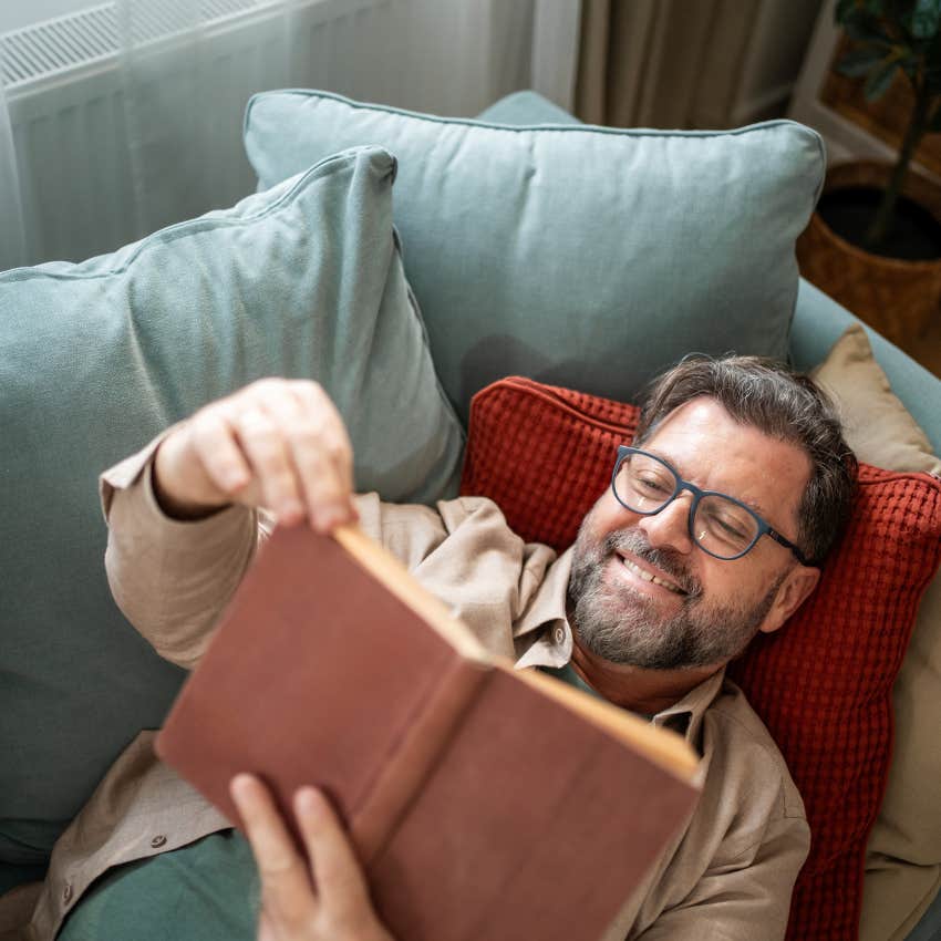 man with quiet intelligence reading a book on his couch
