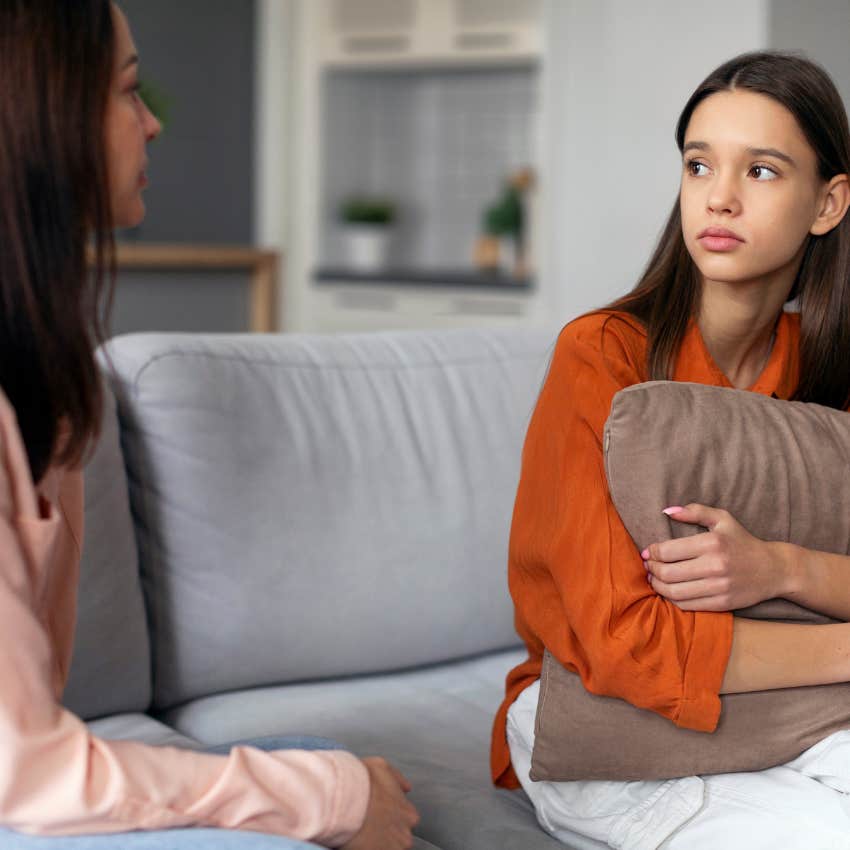 upset teen daughter looking at parent sitting on couch at home