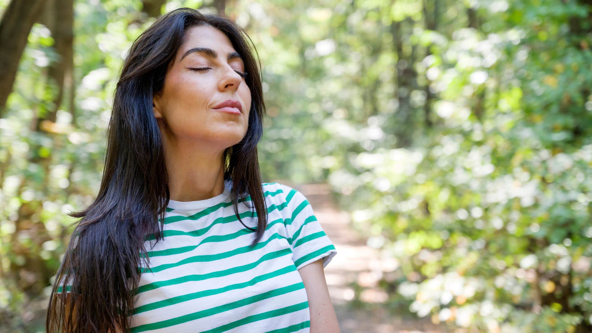 woman in stripped shirt emotionally grounded as she deep breathes outside
