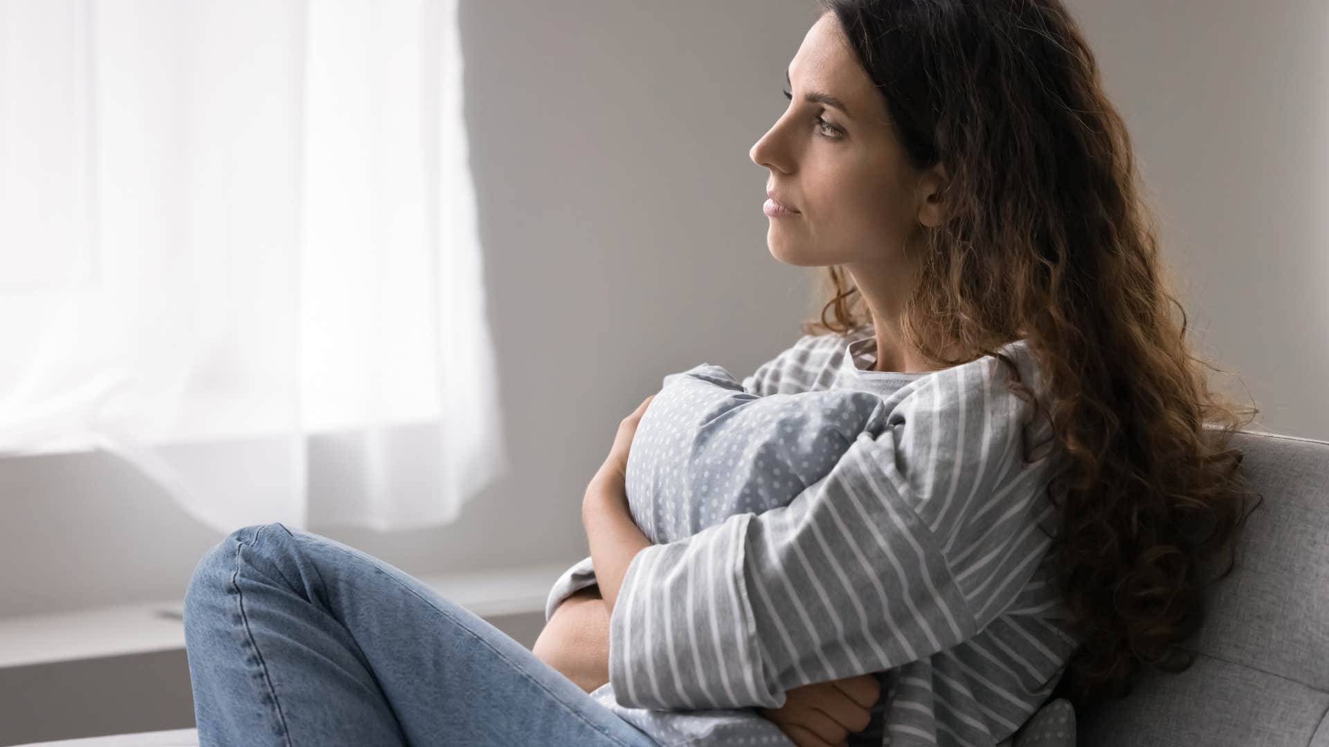 woman thinking deeply and holding pillow tightly as she's feeling sentimental