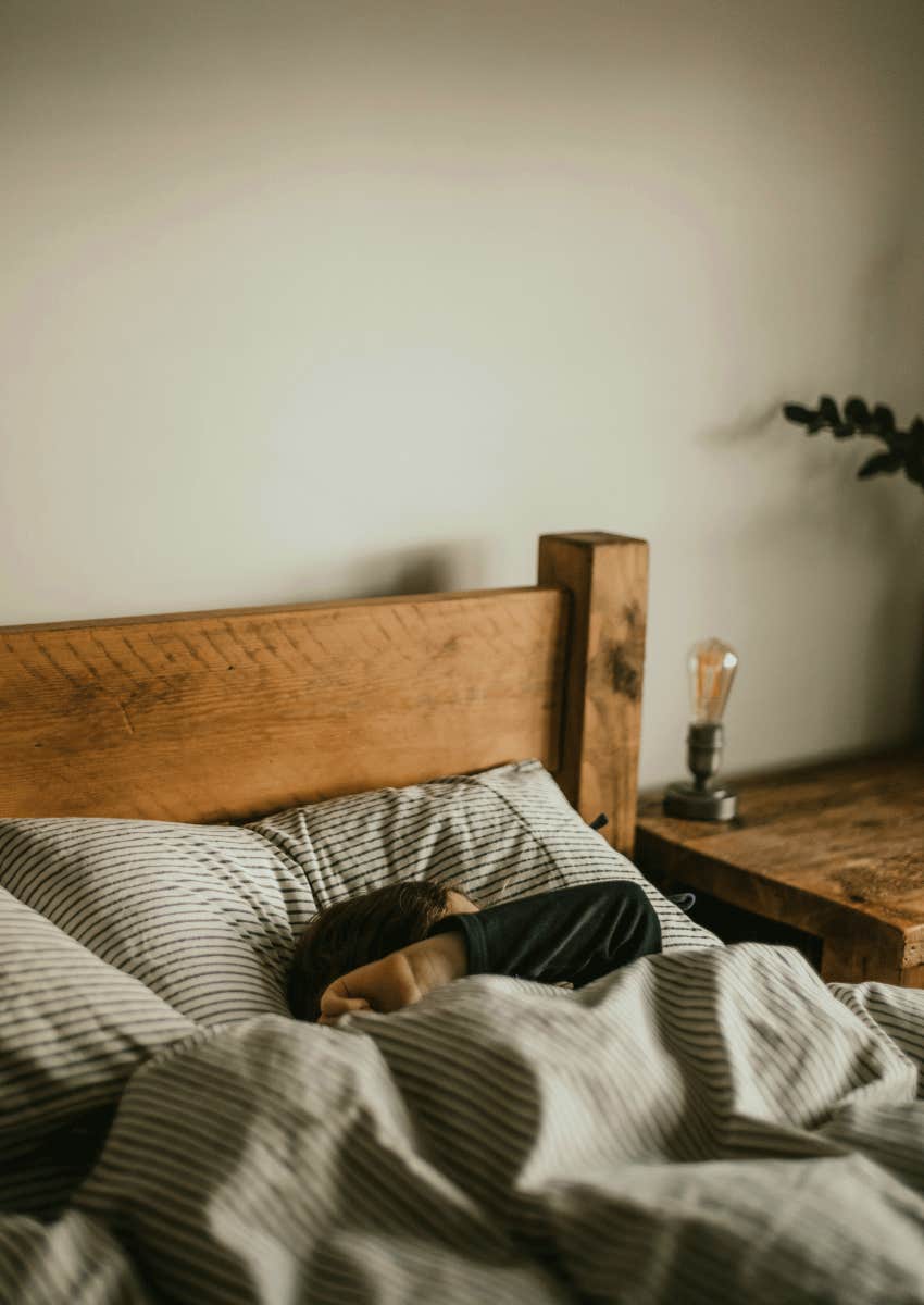 person lying under covers in bed covering face
