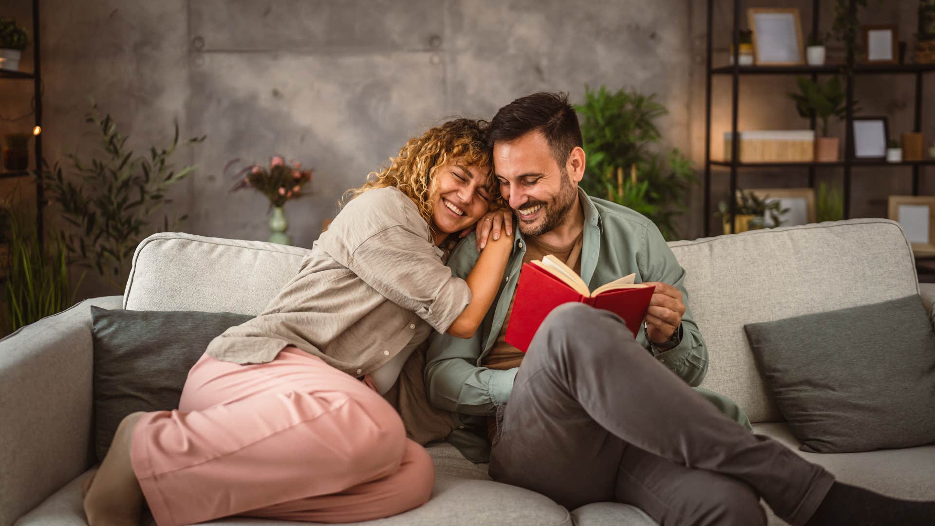 man reading book cuddling with wife on couch