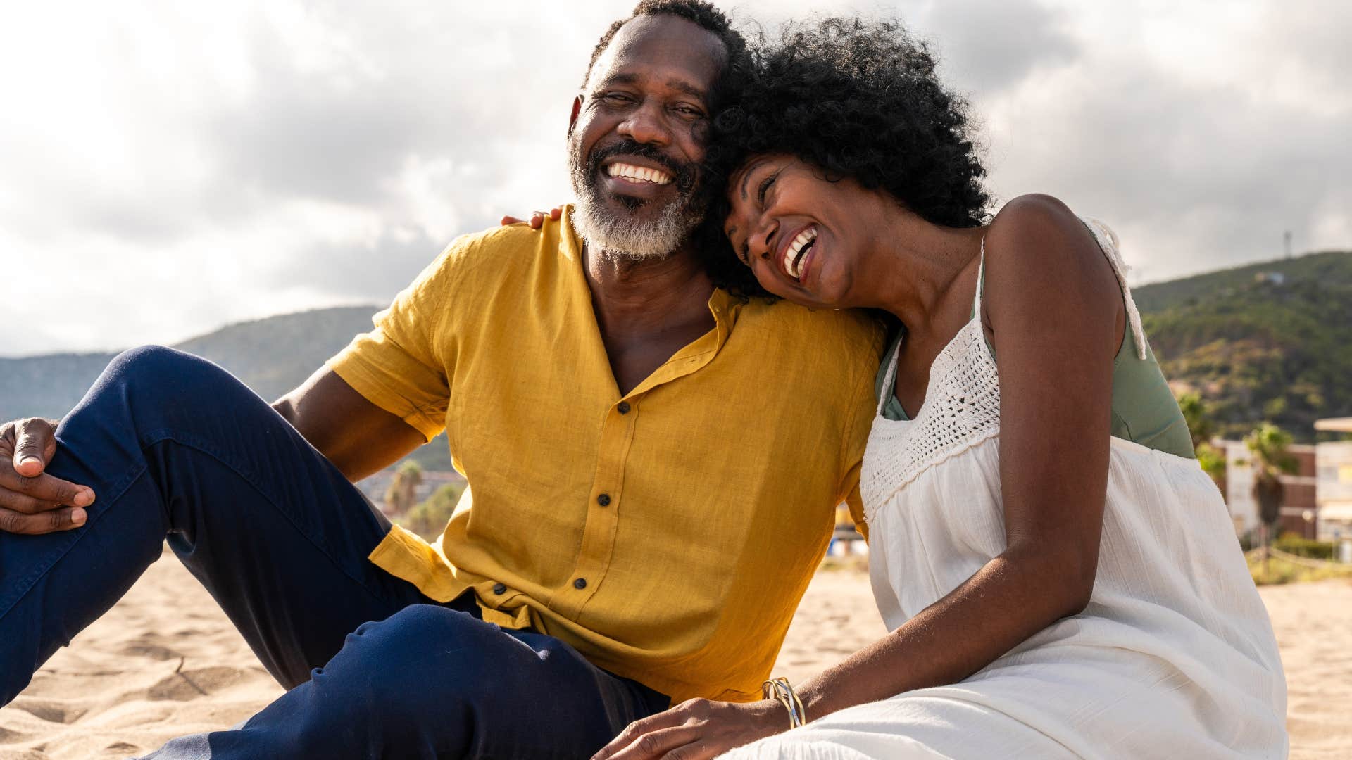 woman leaning head on man's shoulder sitting together on beach