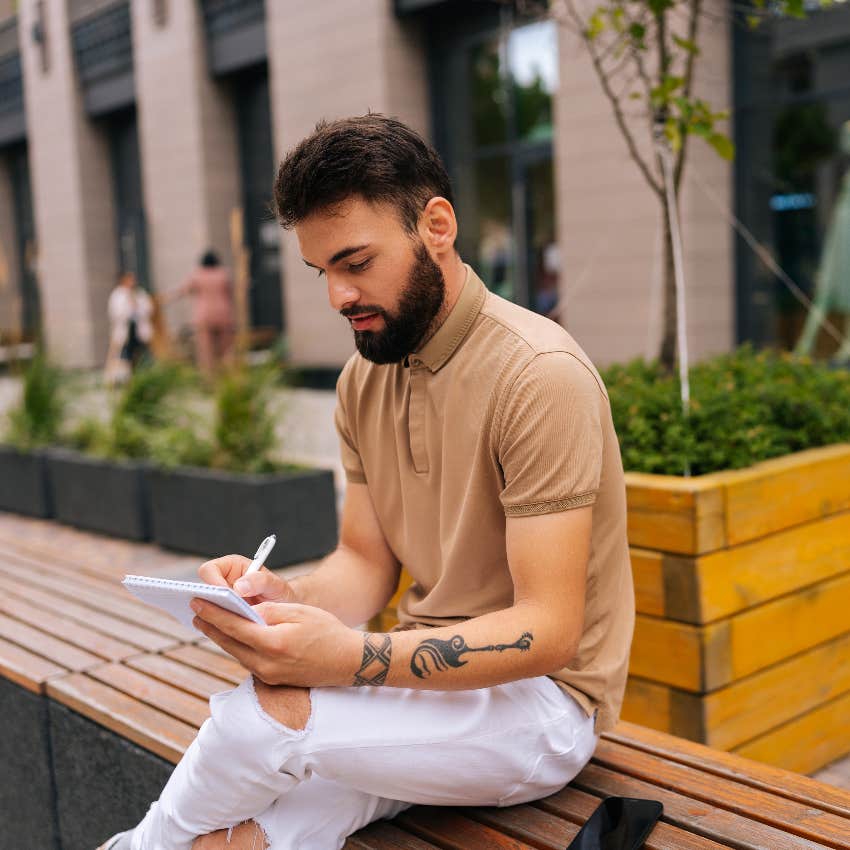 type a man writing schedule in notebook sitting on bench outside