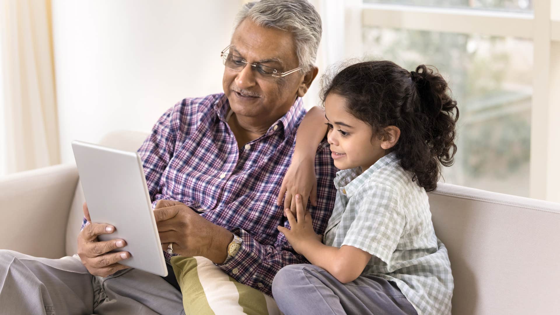 grandfather sitting with granddaughter looking at tablet