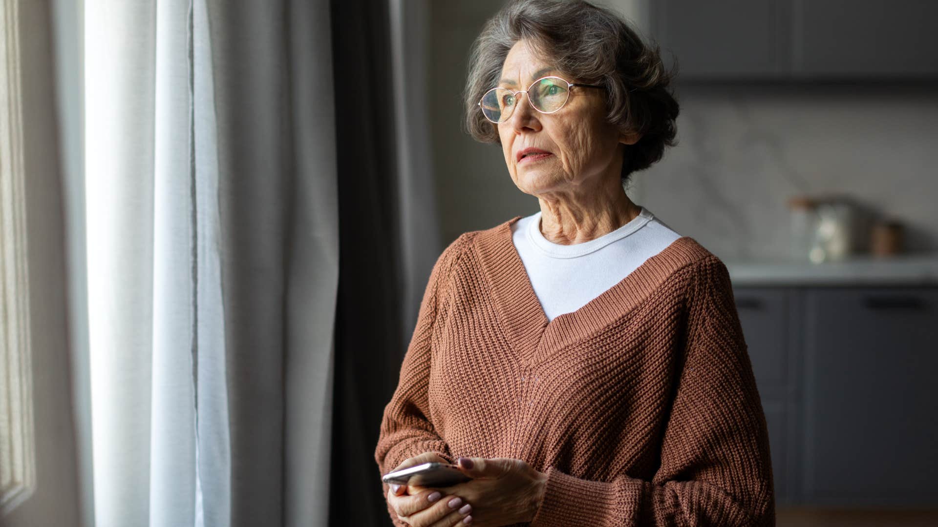 older woman standing near window saying goodbye to version of herself