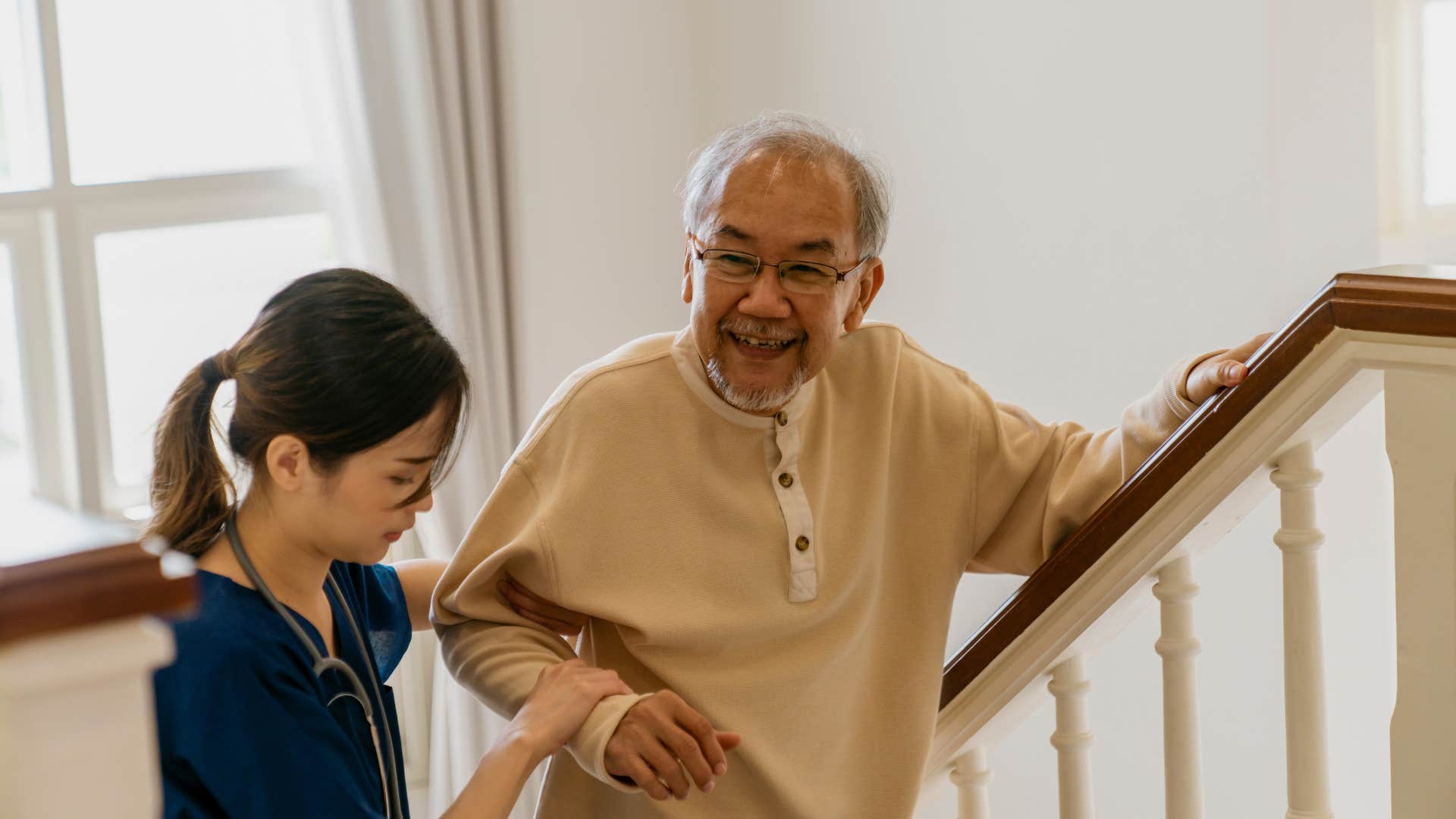 older man being helped up stairs at home by nurse