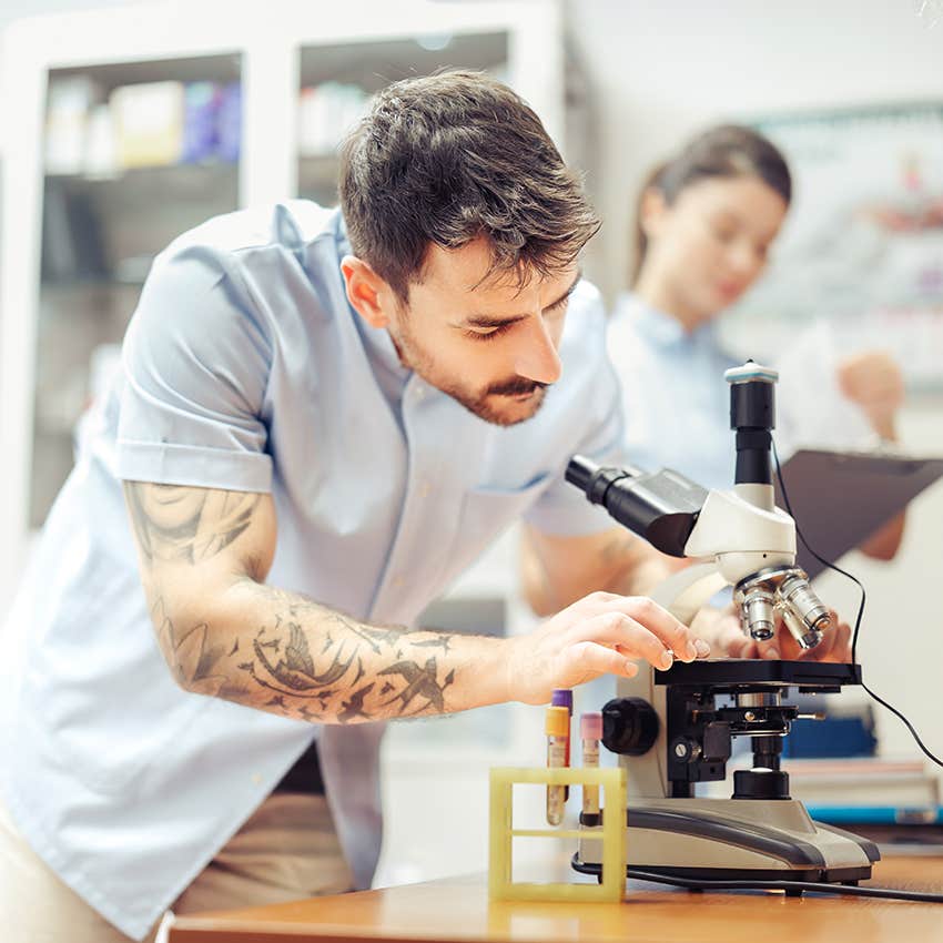 researcher with tattoos looking at microscope