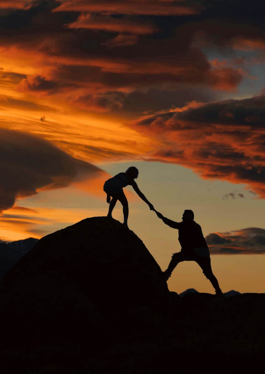 silhouette of successful person helping someone up hill